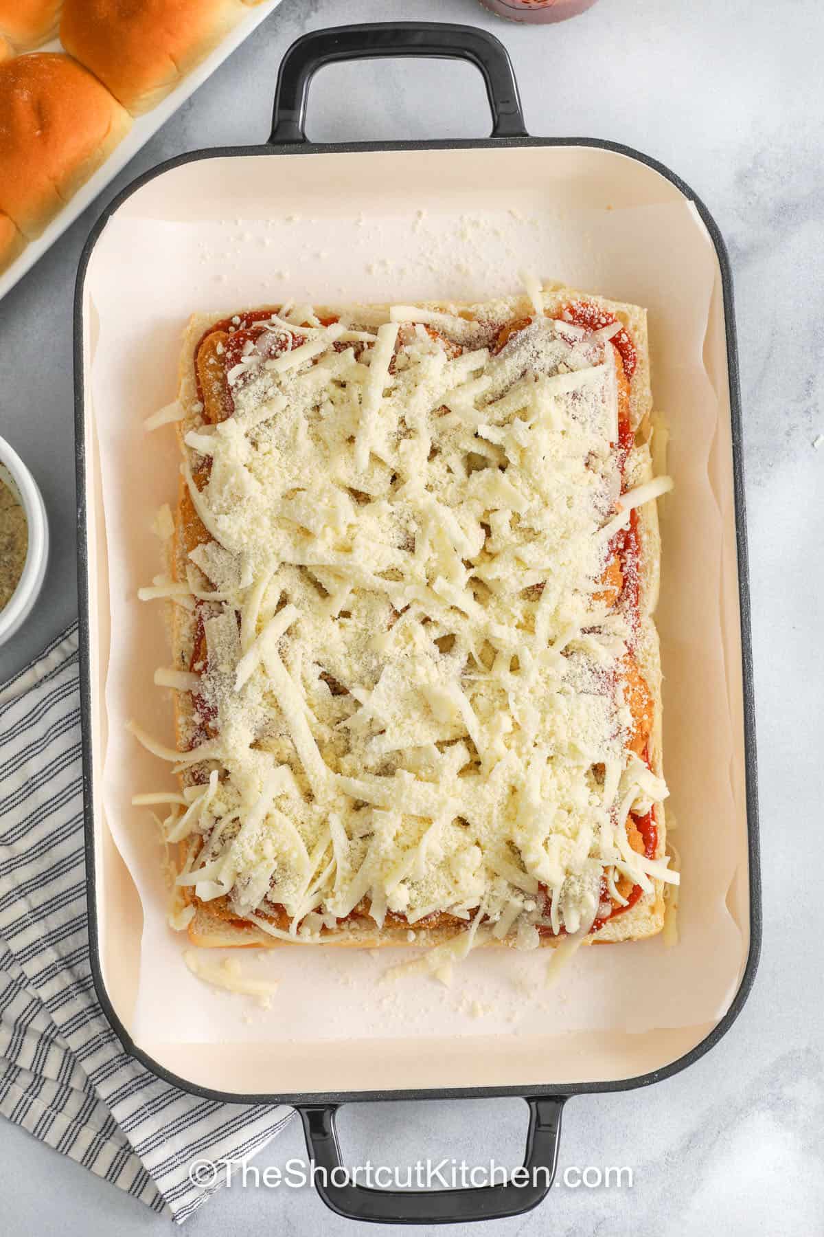 Chicken parm sliders are a crowd-pleasing pull-apart tray. Crispy chicken nuggets, marinara, mozzarella, and parmesan get baked on Hawaiian rolls under a golden garlic butter topping. This easy chicken parm sliders recipe is perfect for parties and weeknights, and you can swap in tenders, Italian blend cheese, or add basil after baking for extra flavor. #theshortcutkitchen chicken parm sliders topped with cheese in a pan