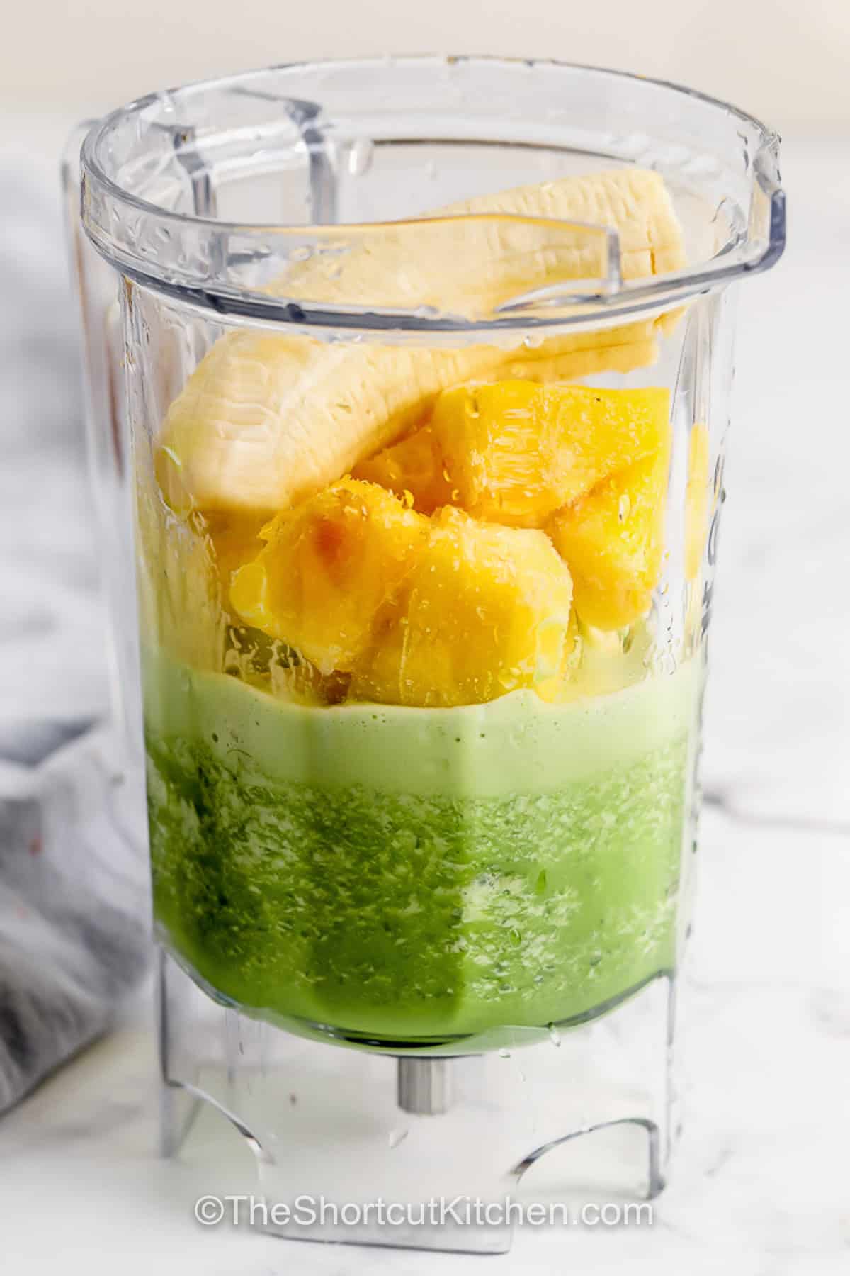 Blend up this Green Smoothie Recipe using simple ingredients like spinach, banana, pineapple, and yogurt. This is a perfect healthy breakfast made in minutes with no chopping needed. Just throw some tasty frozen fruit, fresh or frozen spinach or kale, and any extras you like. Then blend it up in a high speed blender for the perfect breakfast on the go. #theshortcutkitchen ingredients in blender to make Green Smoothie Recipe