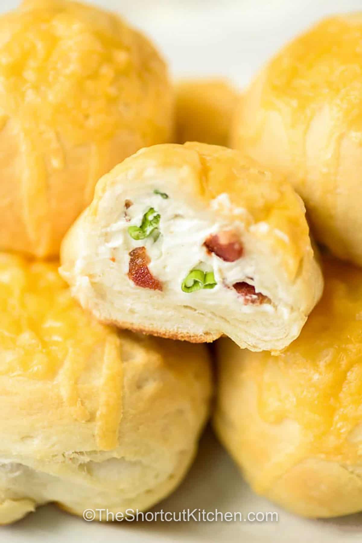 Bacon cream cheese biscuits are the ultimate shortcut stuffed biscuits. Refrigerated biscuit dough gets filled with a creamy mix of bacon, cream cheese, parmesan, green onion, and garlic powder, then topped with cheddar and baked until golden. Perfect for brunch boards, game day snacks, or easy appetizers. Serve warm for the best melty center and flaky bite. #theshortcutkitchen cheesy Bacon Cream Cheese Biscuits on a plate