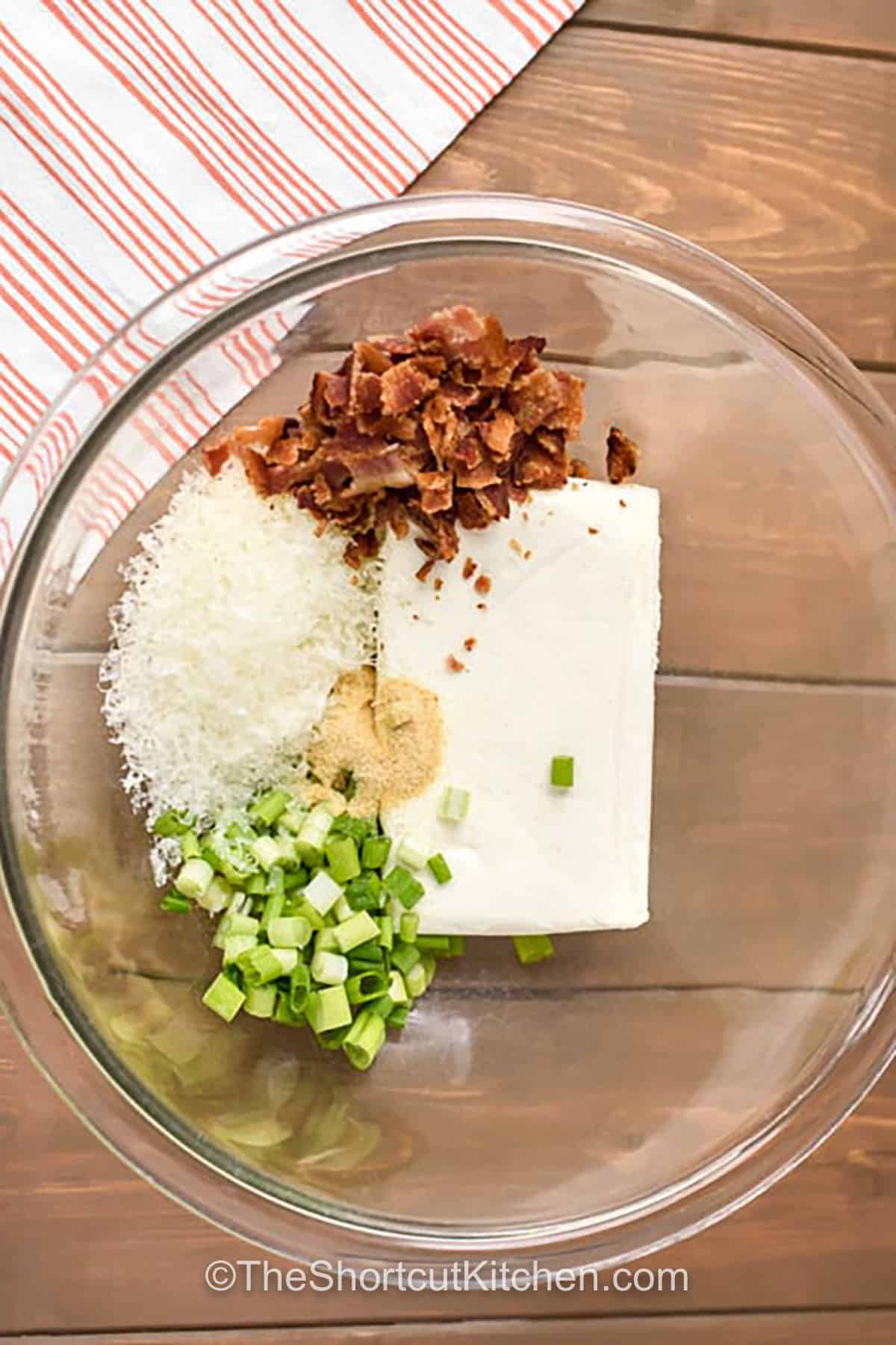 These bacon cream cheese biscuits are easy stuffed biscuits with big comfort-food flavor. Cream cheese, crispy bacon, parmesan, green onion, and garlic powder make a creamy filling, while cheddar melts on top as they bake. Great for holiday brunch, potlucks, and snacky dinners. Keep dough cold for easy sealing and bake until golden brown. #theshortkitchen adding ingredients to cream cheese to make Bacon Cream Cheese Biscuits