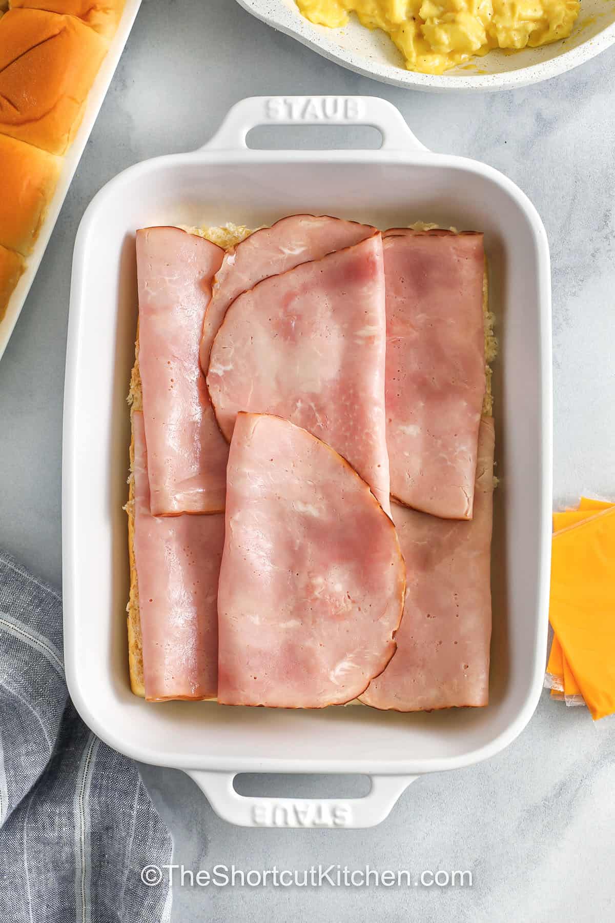 If you need an easy breakfast sandwich that feeds everyone, try breakfast sliders. Hawaiian rolls, fluffy eggs, ham, and cheese bake together fast, and the honey-butter everything topping makes them taste special. Serve for brunch, pack for road trips, or freeze individual sliders for quick mornings. Simple ingredients, big payoff, and minimal cleanup. #theshortcutkitchen adding ham layer to dish to make Breakfast Sliders
