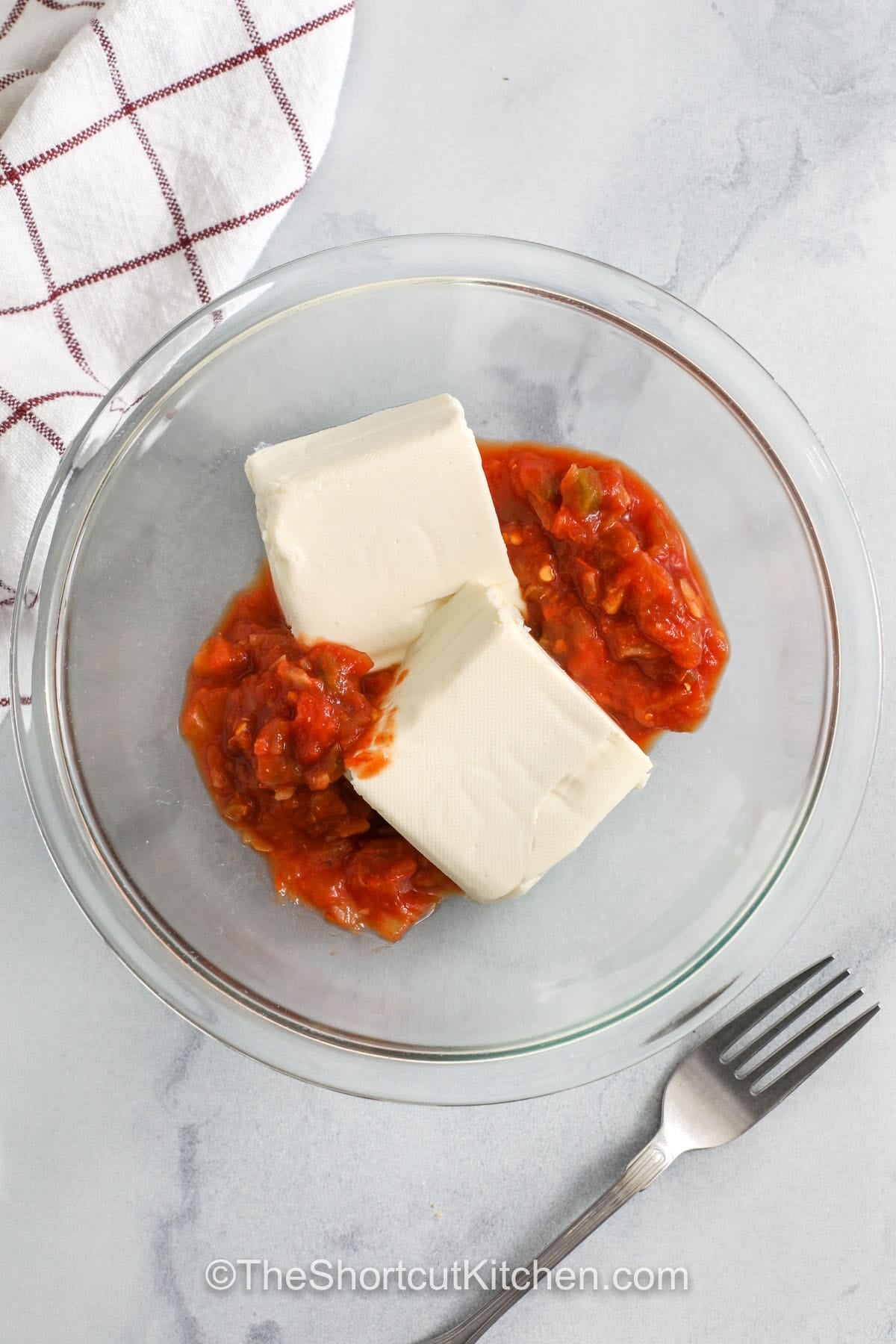 This Cream Cheese Salsa Dip is a no-bake favorite that looks and tastes restaurant-worthy. Mash fully softened cream cheese with salsa until smooth, then chill so it thickens and holds its shape. A chunky salsa works best here. Sprinkle with cheddar cheese and green onions for extra flavor and texture. Stir in diced jalapeños if you want more heat. Serve cold with chips, crackers, or crisp veggie sticks. #theshortcutkitchen adding cream cheese and salsa to bowl to make Cream Cheese Salsa Dip