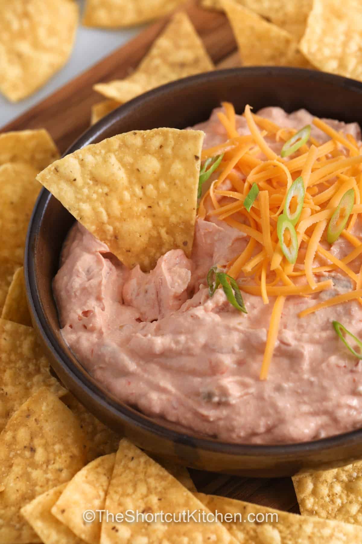 Cream Cheese Salsa Dip is the go-to cold dip for last-minute guests. Cream cheese gives it a rich, creamy base while salsa adds bright flavor. Chilling helps it stay sturdy for easy scooping. Choose a thick, chunky salsa to avoid excess liquid. Top with shredded cheddar cheese and green onions, then add diced jalapeños if you want more spice. This simple two-ingredient dip fits right onto any snack board. #theshortcutkitchen bowl of Cream Cheese Salsa Dip with a tortilla chip in it