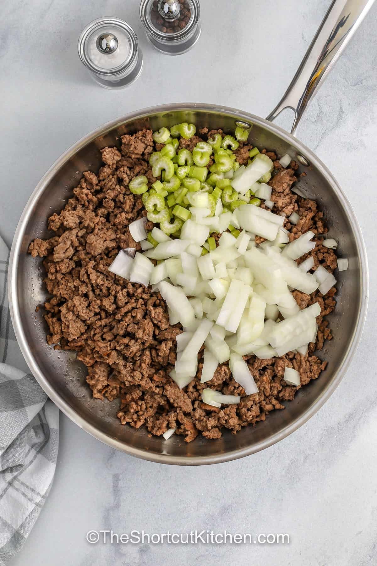 Make hamburger rice casserole when you want comfort food without extra steps. Brown ground beef, then mix it with uncooked long grain rice, condensed cream of chicken soup, cream of mushroom or cream of celery, and milk for a creamy ground beef and rice casserole. Bake covered until tender, then top with cheddar cheese. Optional mushrooms work great, but it’s still delicious without them. #theshortcutkitchen adding onions and celery to ground beef to make Hamburger Rice Casserole