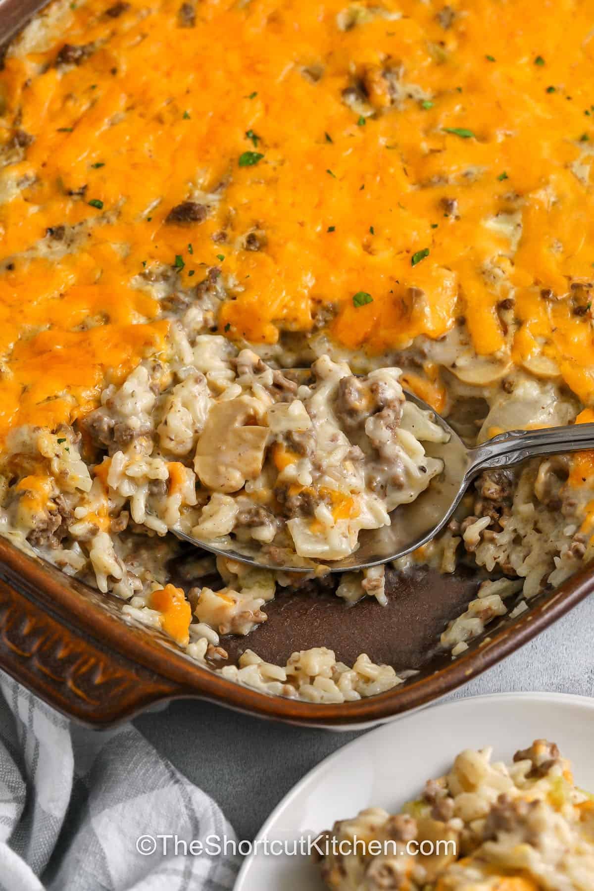 Classic comfort food with shortcut ingredients. This hamburger rice casserole uses ground beef, onion, celery, uncooked long grain rice, condensed cream soups, and milk to create a creamy baked casserole with minimal prep. Finish with shredded cheddar cheese for a melty top. It’s an old fashioned hamburger rice casserole that tastes like home and reheats great. #theshortcutkitchen Hamburger Rice Casserole in the dish and on a spoon