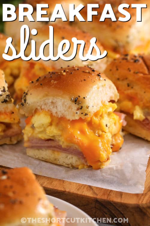 Ham egg and cheese breakfast sliders are a cozy, satisfying breakfast that slices perfectly. Keep rolls attached, soft-scramble the eggs, and layer everything in a pan. The buttery everything bagel seasoning topping with a touch of honey makes the tops golden and irresistible. Great for make ahead breakfasts, holiday mornings, and feeding hungry teens. #theshortcutkitchen platter of Breakfast Sliders with a title