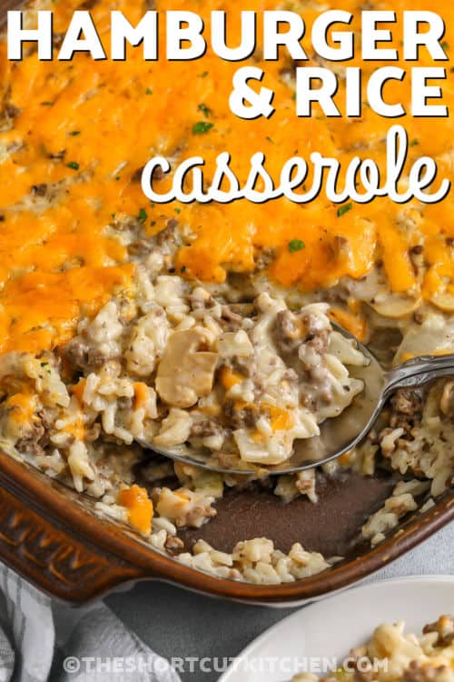 This cheesy hamburger casserole is a total dinner win. Hamburger rice casserole combines browned ground beef with onion and celery, then mixes with uncooked rice, condensed cream soups, and milk for a creamy, cozy bake. Sprinkle shredded cheddar cheese on top to finish. It’s an easy weeknight casserole that’s budget-friendly, family-size, and simple to customize with veggies. #theshortcutkitchen taking a spoonfull of Hamburger Rice Casserole out of the dish with writing