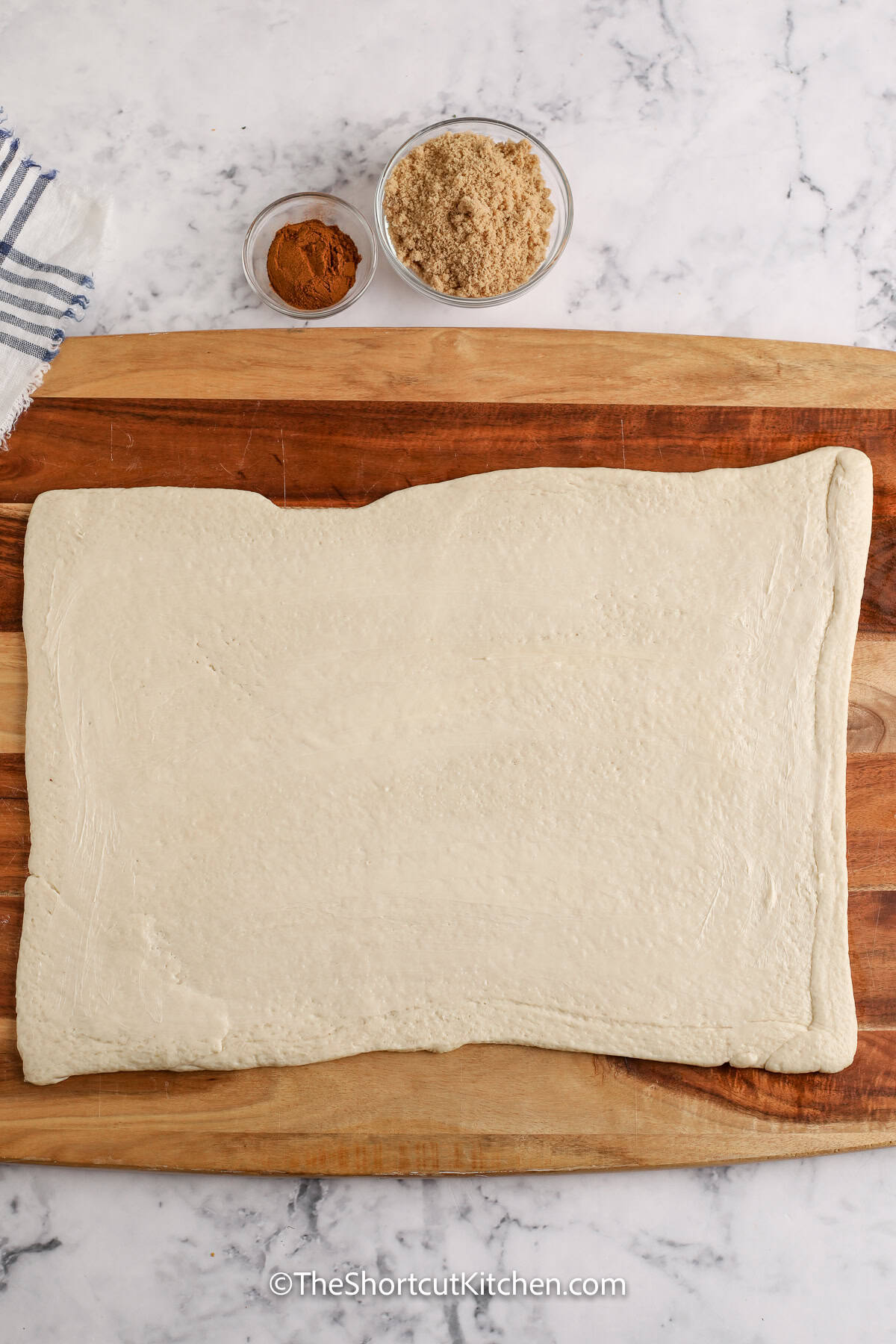 Pizza Dough Cinnamon Rolls are the ultimate shortcut breakfast. Use Pillsbury pizza dough or swap in crescent roll dough. Spread softened butter, add brown sugar and cinnamon, roll, slice, and bake in a 9×9 pan until golden. Finish with a quick cinnamon roll glaze for warm, cinnamon roll comfort that’s ready to enjoy in under an hour. #theshortcutkitchen pizza dough rolled out to make Pizza Dough Cinnamon Rolls