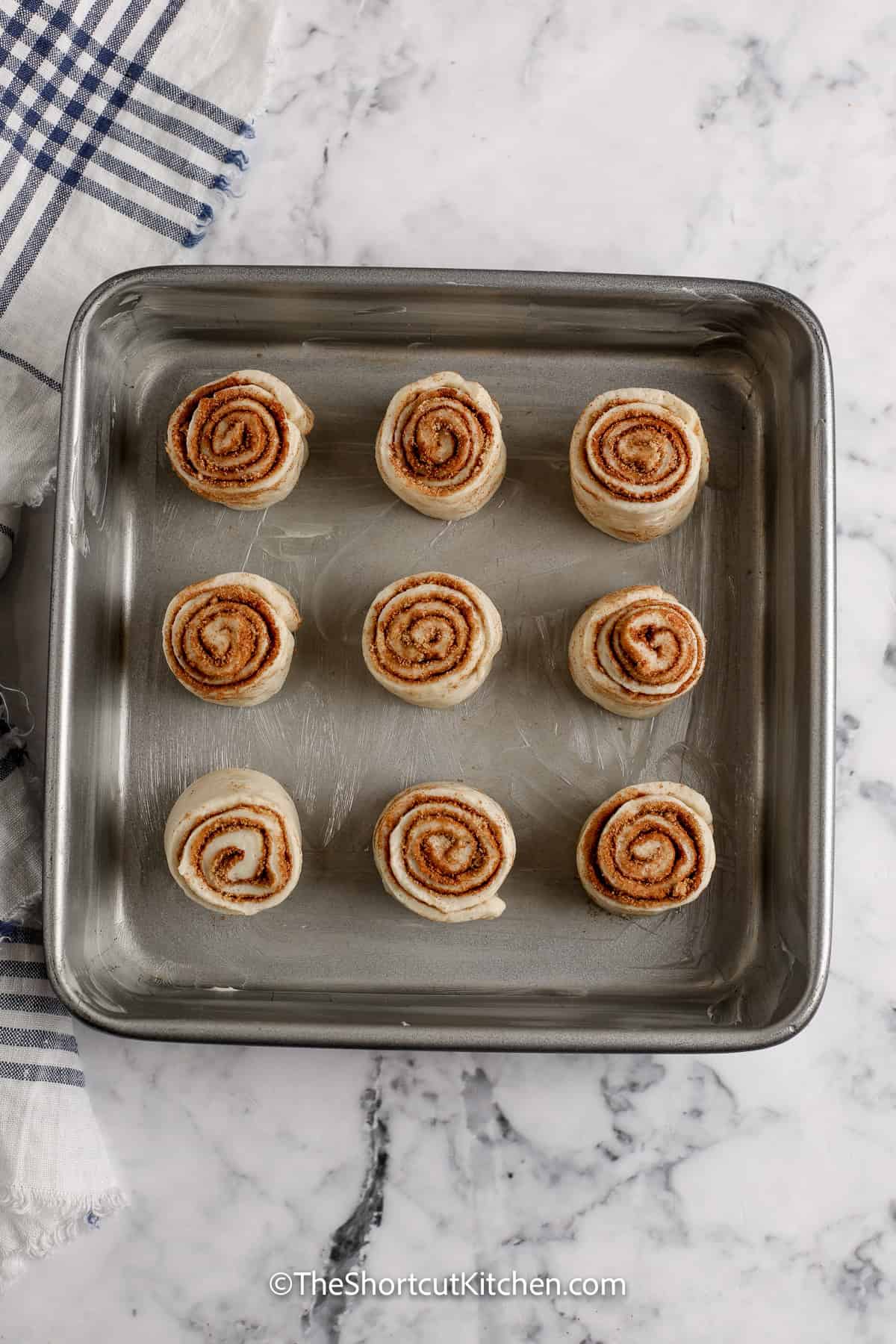 Pizza Dough Cinnamon Rolls are perfect for busy mornings. Use refrigerated dough or crescent roll cinnamon rolls dough, spread butter, top with cinnamon and brown sugar, then roll tight and slice cleanly. Bake until golden and add a quick cinnamon roll glaze. Warm, sweet, and ready in under an hour. #theshortcutkitchen Pizza Dough Cinnamon Rolls in a baking pan