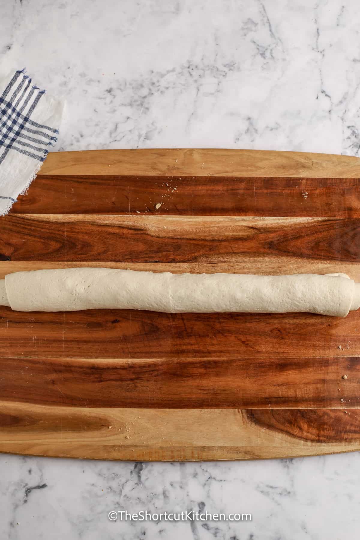 These Pizza Dough Cinnamon Rolls use Pillsbury-style dough, cinnamon, butter, and brown sugar for sweet, delicious cinnamon spirals. Bake in a 9×9 pan so they stay soft. Finish with a quick powdered sugar glaze, or keep them plain. These are so delicious served warm and fresh out of the oven. Perfect with a cup of coffee in the morning. #theshortcutkitchen rollled up Pizza Dough Cinnamon Rolls before slicing and baking