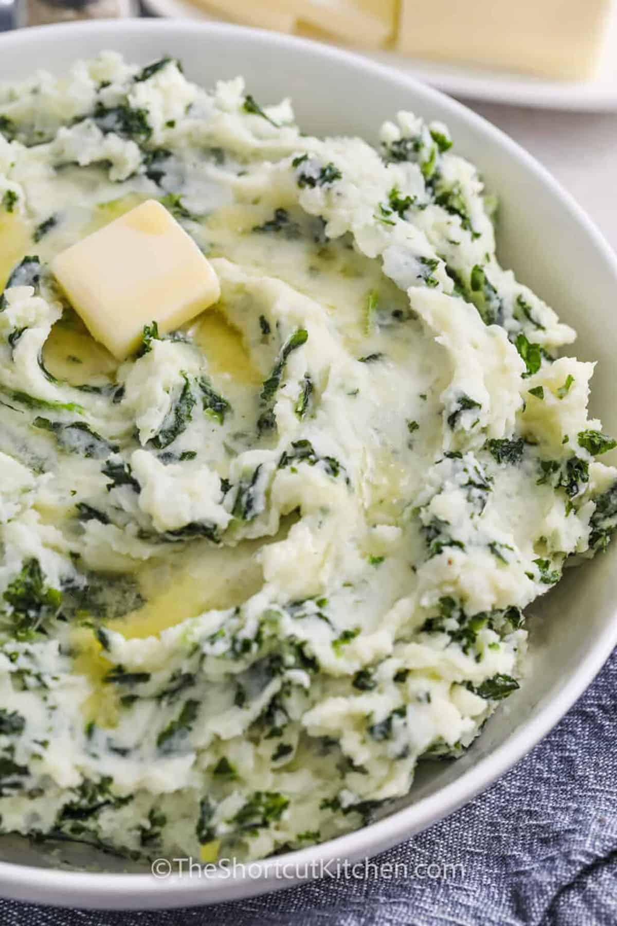 Make classic Irish mashed potatoes at home with this easy colcannon recipe. Baking potatoes mash up creamy with warm heavy cream and butter, then you stir in buttery onions and frozen kale for a quick weeknight-friendly twist. This mashed potatoes with kale side dish is perfect for St. Patrick’s Day or any cozy dinner, and it reheats beautifully with a splash of cream. #theshortcutkitchen plated Colcannon with butter