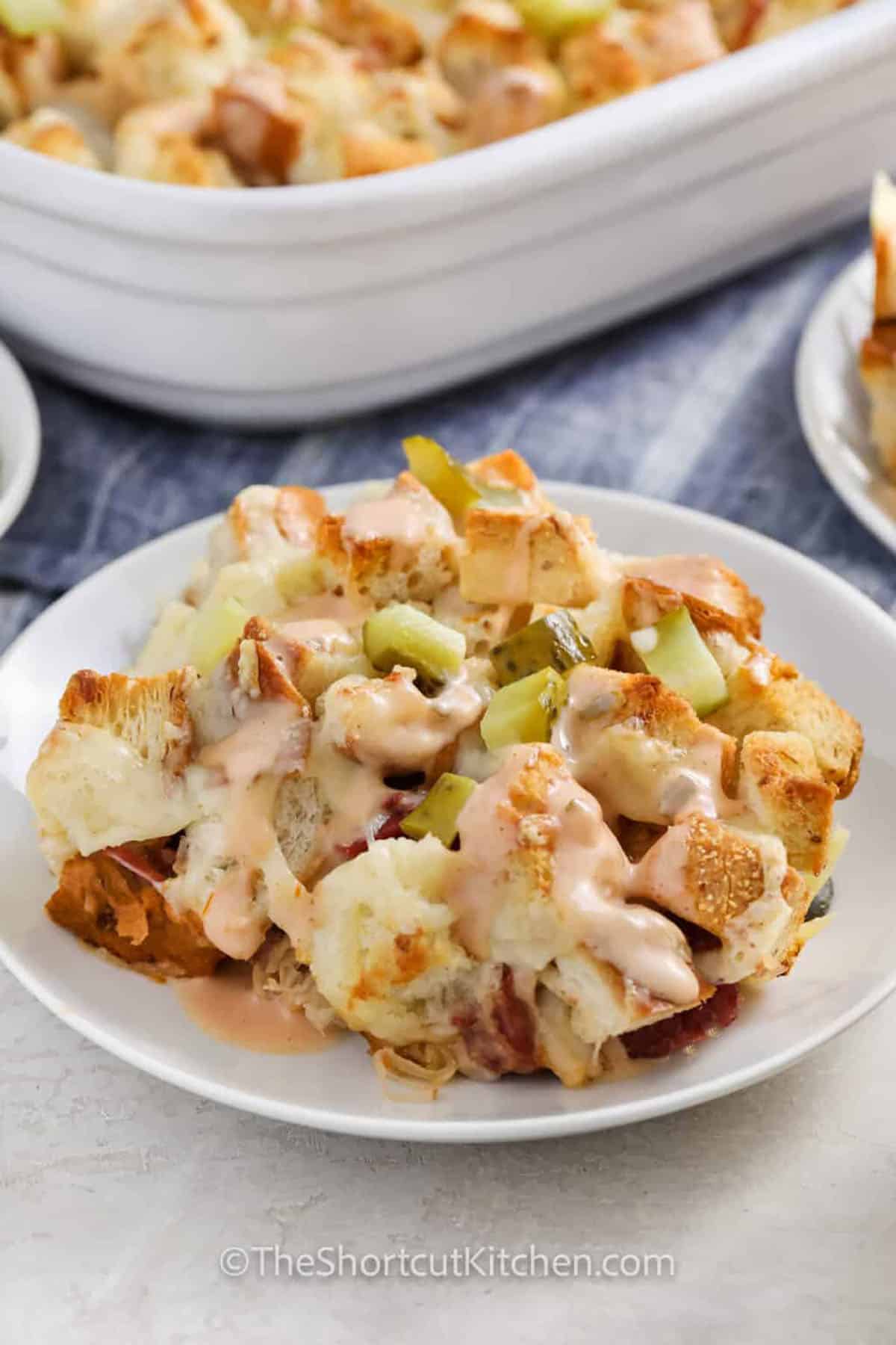 Love Reuben sandwiches? You’ll love this baked Reuben casserole. Rye bread cubes, corned beef, sauerkraut, Swiss cheese, and Thousand Island dressing layer into a bubbly, cozy Reuben casserole that’s great for parties or weeknight dinners. Finish with chopped pickles for the classic bite. A simple, oven-baked comfort meal. #theshortcutkitchen plated Reuben Casserole with casserole dish full in the back