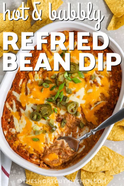Refried bean dip is a warm and cheesy party favorite that always disappears fast. This easy baked bean dip blends refried beans, salsa, taco seasoning, and sour cream for bold Tex-Mex flavor in every bite. Melted Mexican cheese on top makes it perfect for tortilla chips or crackers. Serve this hot bean dip at game-day parties, potlucks, or family movie nights when you want a simple appetizer everyone will reach for again and again. #theshortcutkitchen hot and bubbly Refried Bean Dip with writing