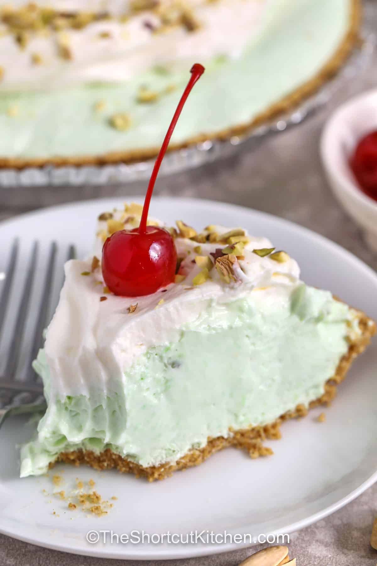 Make this pistachio pie when you need a quick, chilled dessert. This no bake pistachio pie uses instant pistachio pudding, milk, cream cheese, and whipped topping for a smooth, airy pistachio pudding pie that sets up beautifully in the fridge. Spoon into a graham crust, chill, and garnish with pistachios or cherries. Great for potlucks, holidays, and summer BBQs. #theshortcutkitchen close up of a slice of Pistachio Pie with a bite taken out