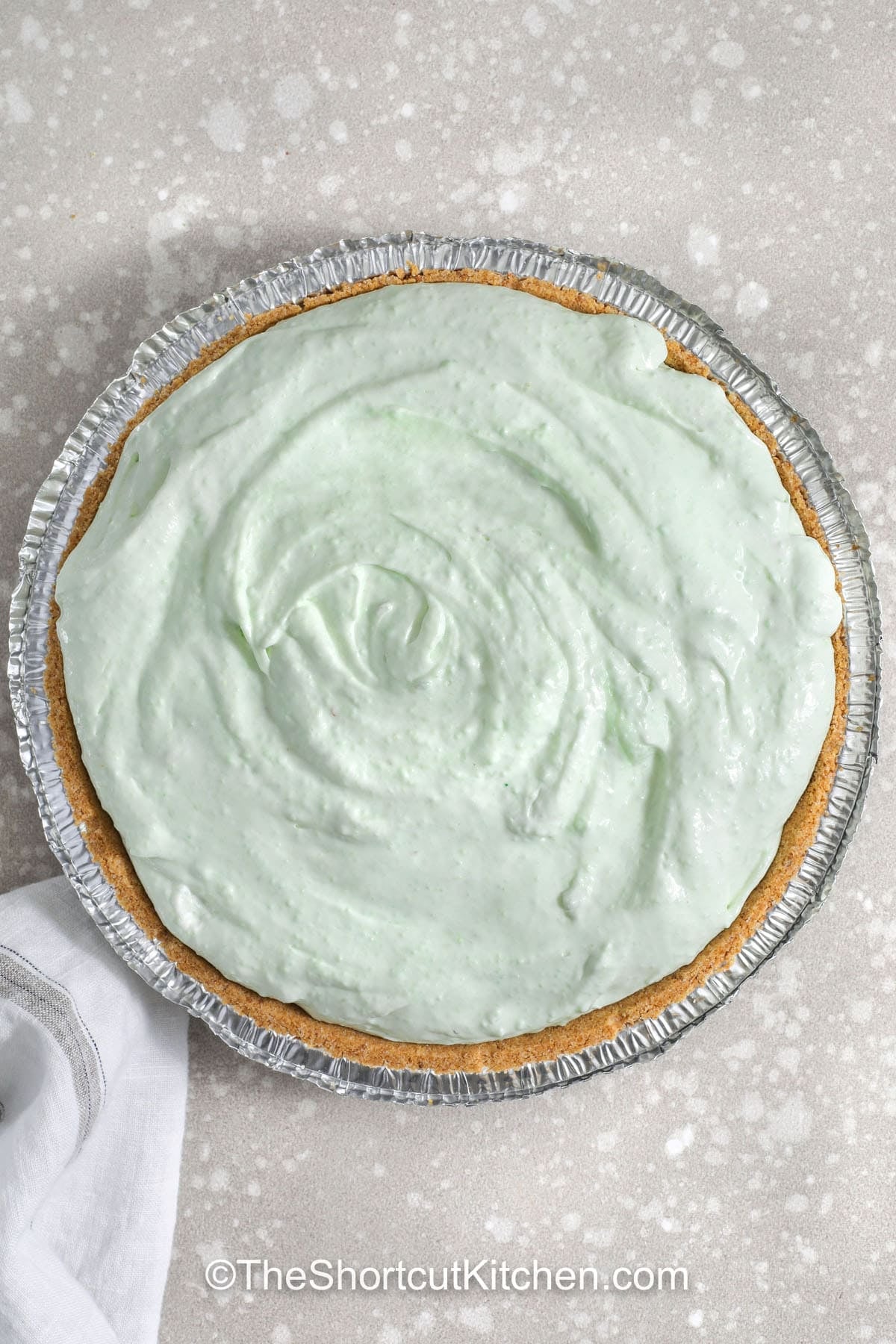 Pistachio pie is a classic, shortcut-friendly dessert that tastes rich but feels light. Instant pistachio pudding mix and cold milk create the base, cream cheese adds a tangy cheesecake note, and Cool Whip keeps the filling airy. Spread into a graham cracker crust and chill until firm. This pistachio pudding pie is made for parties and easy make-ahead weekends. #theshortcutkitchen adding filling to graham cracker crust to make Pistachio Pie