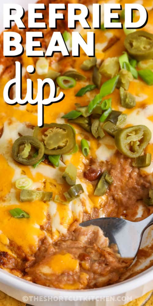 Refried bean dip makes a warm and satisfying appetizer that is perfect for sharing. This easy Tex-Mex dip combines refried beans, salsa, sour cream, and taco seasoning with plenty of melted cheese on top. Serve this baked bean dip with tortilla chips or fresh veggies for a simple party snack. It is a great choice for game day food, potluck dishes, or casual get-togethers when you need a hot dip recipe that comes out just right every time you make it at home. #theshortcutkitchen taking a spoonfull of Refried Bean Dip out of dish with a title
