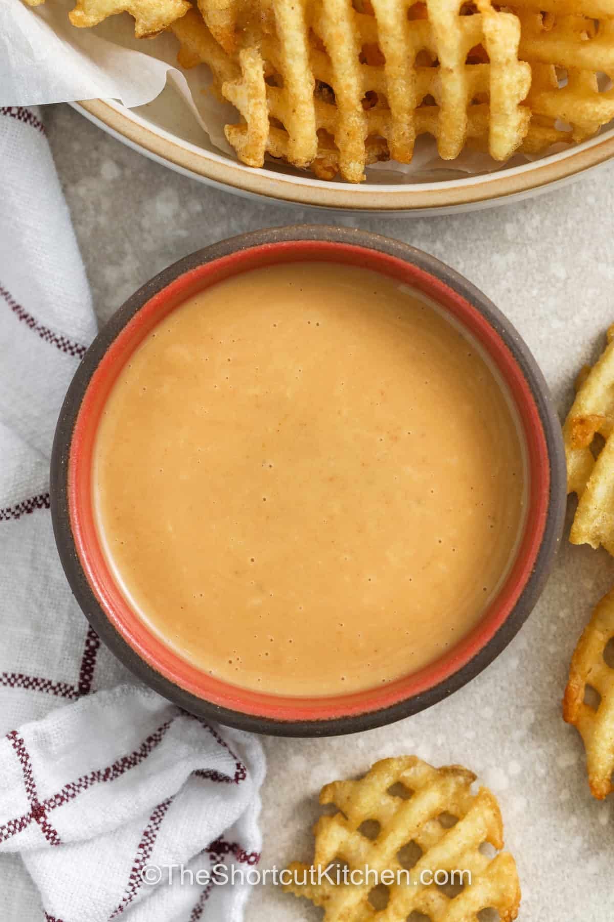 Chick-Fil-A sauce recipe lovers will enjoy this easy homemade version that brings that sweet, smoky, and tangy flavor right to your kitchen. Made with simple pantry ingredients like mayo, BBQ sauce, and honey, this copycat Chick-Fil-A sauce recipe is perfect for dipping chicken nuggets, fries, or spreading on sandwiches. It blends smoothly and is creamy every time for a bold flavor boost to any meal. #theshortcutkitchen top view of chick-fil-a sauce recipe with some waffle style french fries in the background