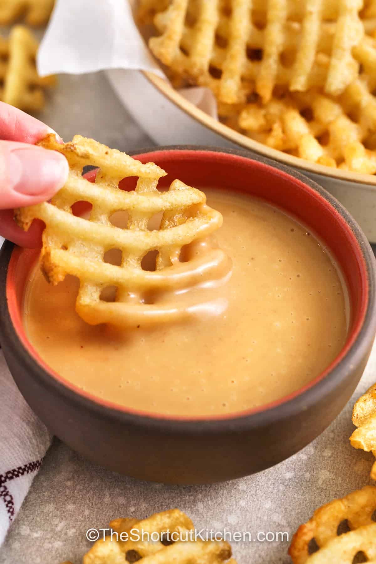 Chick-Fil-A sauce recipe is a must-have for dipping, and this homemade version makes it easy to enjoy anytime. This copycat Chick-Fil-A sauce recipe combines mayo, honey, mustard, and BBQ sauce for a smooth and creamy dip with sweet and smoky flavor. It is perfect for chicken tenders, fries, or even as a sandwich spread. Keep a batch on hand to add extra flavor to meals and snacks without needing a trip out. #theshortcutkitchen dipping a waffle fry into a bowl of chick-fil-a sauce recipe