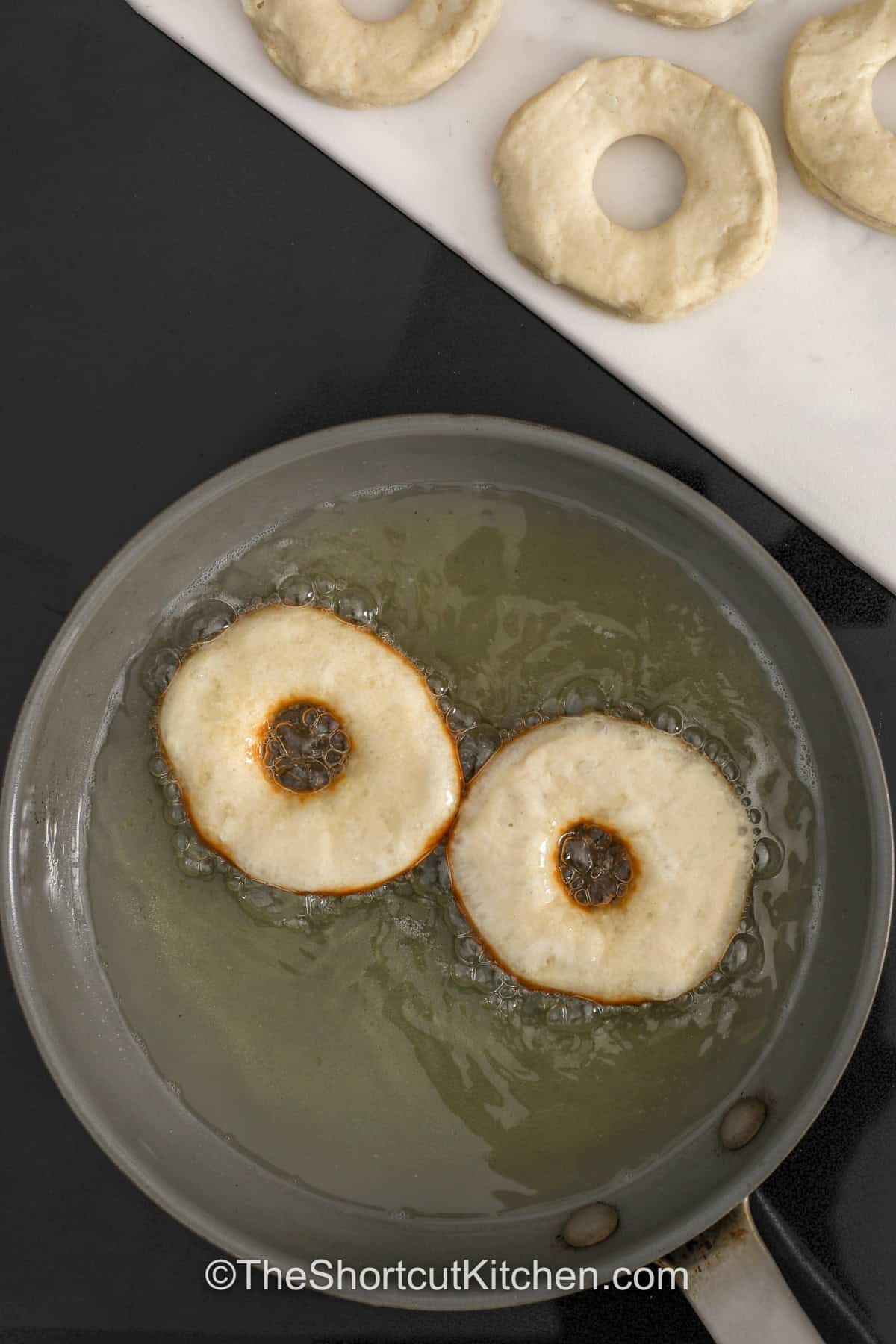 This easy donut recipe is a shortcut win: biscuit donuts made with refrigerated canned biscuits, fried quickly and coated in buttery cinnamon sugar. Keep it classic or dip in vanilla glaze or chocolate glaze once they cool slightly. Donut holes cook even faster, making this perfect for kids and busy mornings. Air fryer donuts method included. #theshortcutkitchen 2 donuts in oil