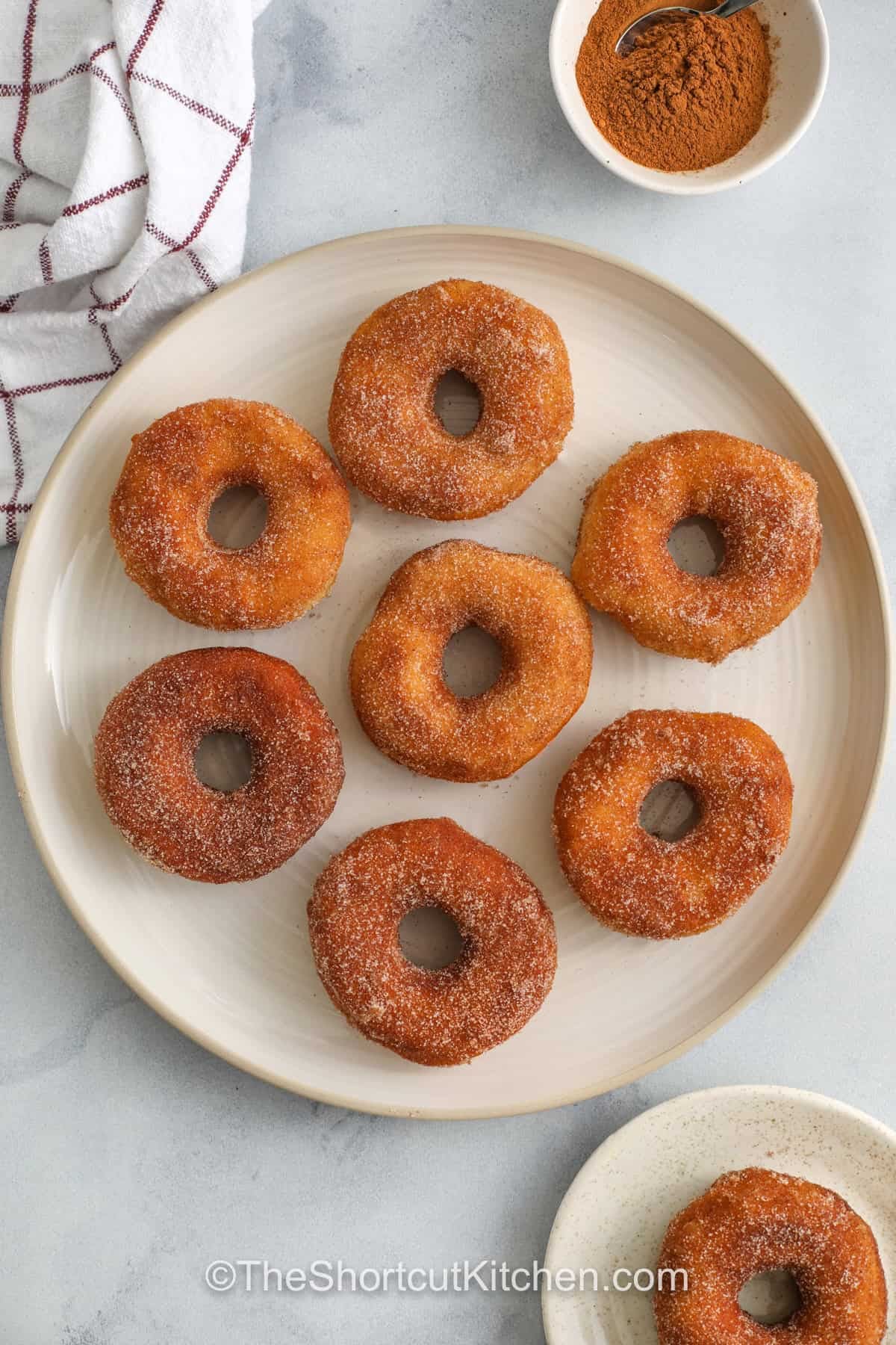 Craving cinnamon sugar donuts? This easy donut recipe uses refrigerated biscuit dough to make canned biscuit donuts in about 25 minutes. Cut donut rings and donut holes, fry until golden, and toss in cinnamon sugar while warm so it sticks. Add vanilla glaze or chocolate glaze for a bakery-style finish. Air fryer donuts directions included. #theshortcutkitchen top view of seven donuts on a white plate