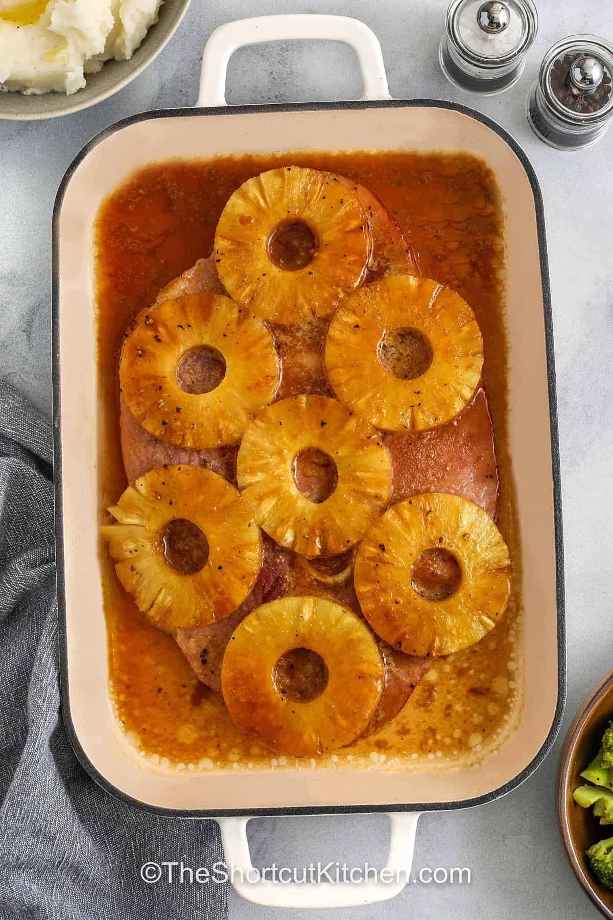 This ham steak recipe is baked with pineapple and creates a delicious dinner that everyone will enjoy. The ham steak is topped with pineapple rings and covered in a sweet brown sugar glaze that caramelizes in the oven. Dijon mustard and soy sauce add a savory depth that balances the sweetness. This recipe works well for a weeknight dinner or a small holiday meal. Serve it with mashed potatoes, rice, or roasted vegetables for a complete meal. #theshortcutkitchen baked Ham Steak in the dish with pineapple rings