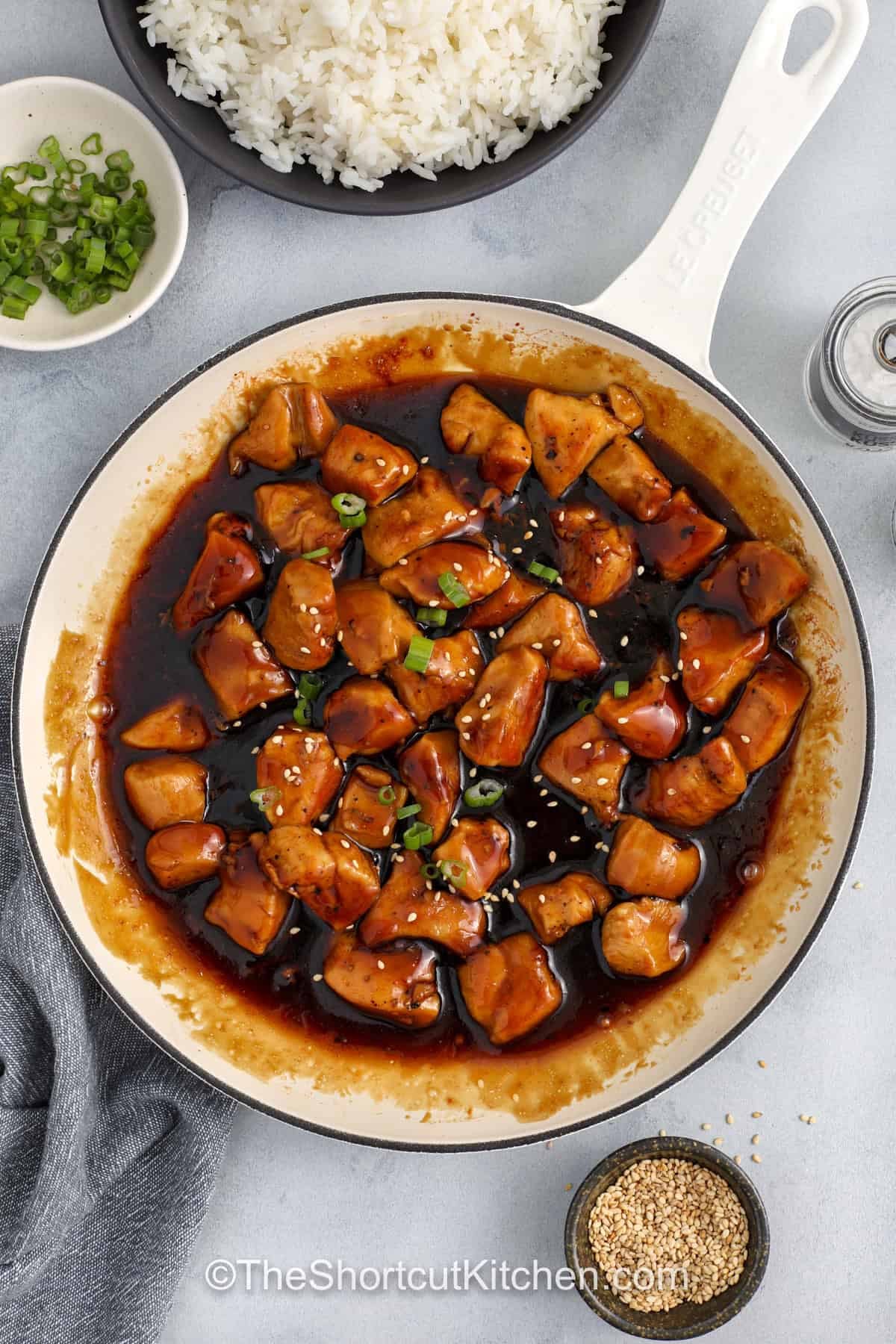 Honey teriyaki chicken brings classic sweet and savory flavor to an easy skillet dinner. Tender chicken bites simmer in a homemade honey teriyaki sauce made with bottled teriyaki, honey, garlic, and rice vinegar. The sauce thickens into a rich glaze that coats each piece of chicken with bold flavor. This simple chicken dinner pairs well with rice, noodles, or vegetables for a satisfying meal made with pantry staples and fresh garnishes like sesame seeds and green onions. #theshortcutkitchen cooked Honey Teriyaki Chicken in a pan