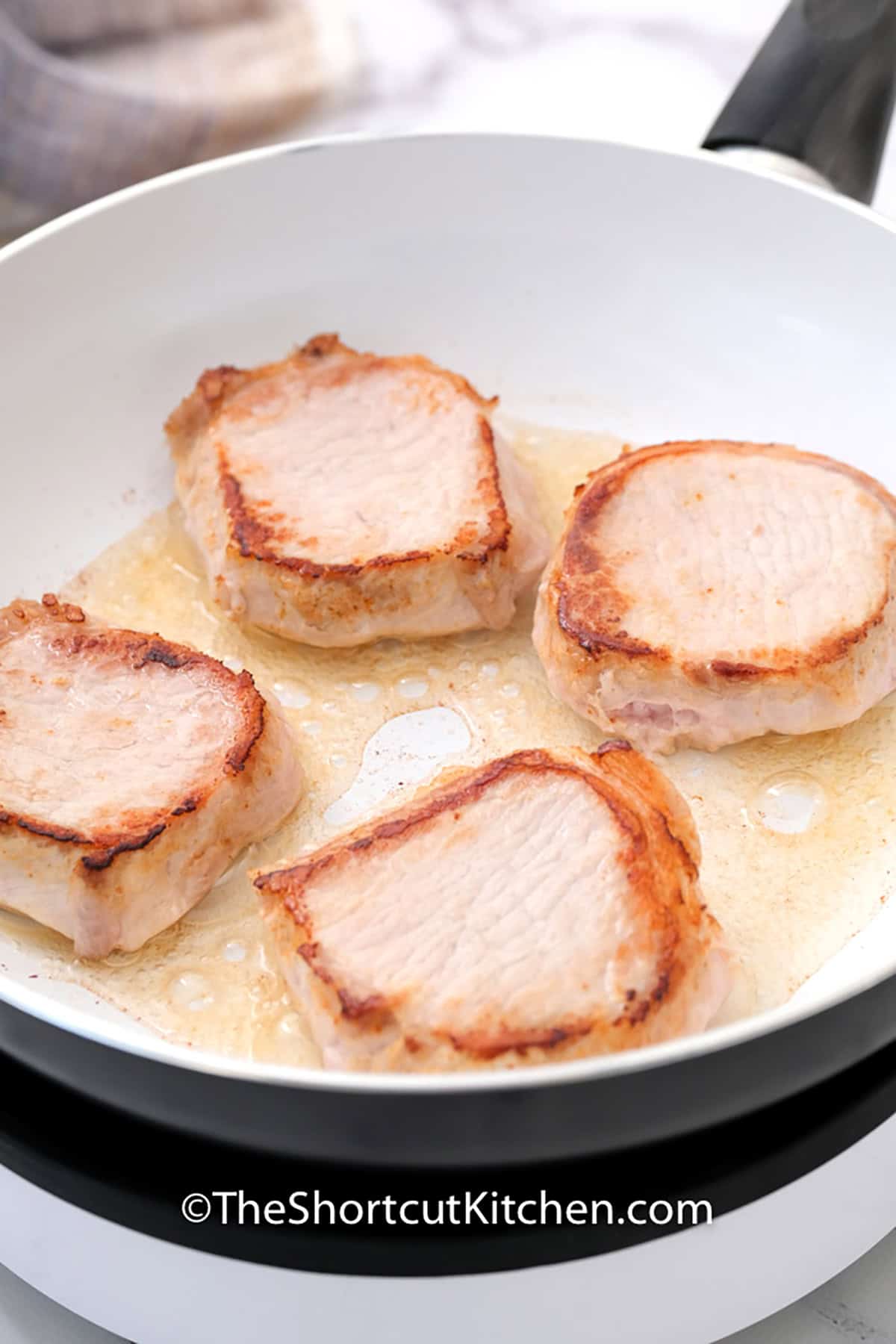 Short on time but craving something homemade? Try this smothered pork chops recipe. Using only 5 ingredients including thick pork chops and stuffing mix, this dish is prepped in 10 minutes and baked to golden perfection. It is the perfect solution for a cozy family dinner. #theshortcutkitchen pork chops cooking in a pan to make Smothered Pork Chops Recipe