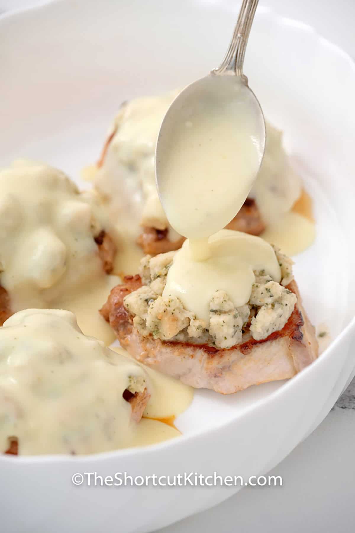 This smothered pork chops recipe is the ultimate shortcut dinner. We use a simple stuffing mix and condensed soup to create a rich gravy and flavorful topping for thick-cut pork. It is a one-pan style bake that brings all the flavor of a holiday meal to your Tuesday night. #theshortcutkitchen adding sauce to pork chops to make Smothered Pork Chops Recipe