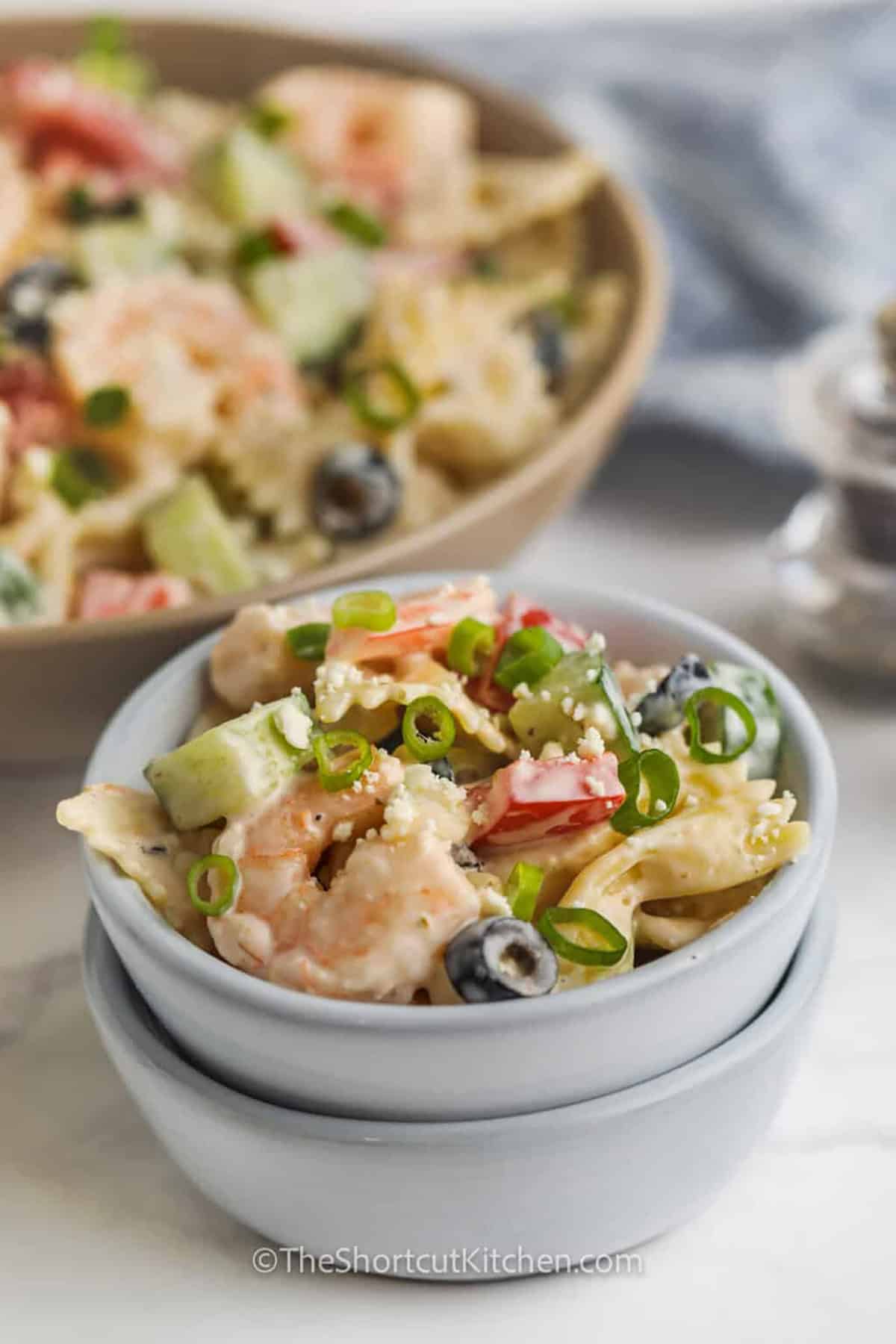Greek shrimp pasta salad is a simple shrimp pasta salad recipe that delivers big flavor with little effort. Tender penne or farfalle, cool cucumber, juicy tomatoes, salty feta, and olives are mixed in a creamy Greek-style dressing for a chilled salad that is fresh, filling, and ideal for hot days. #theshortcutkitchen tangy Greek Shrimp Pasta Salad in a bowl