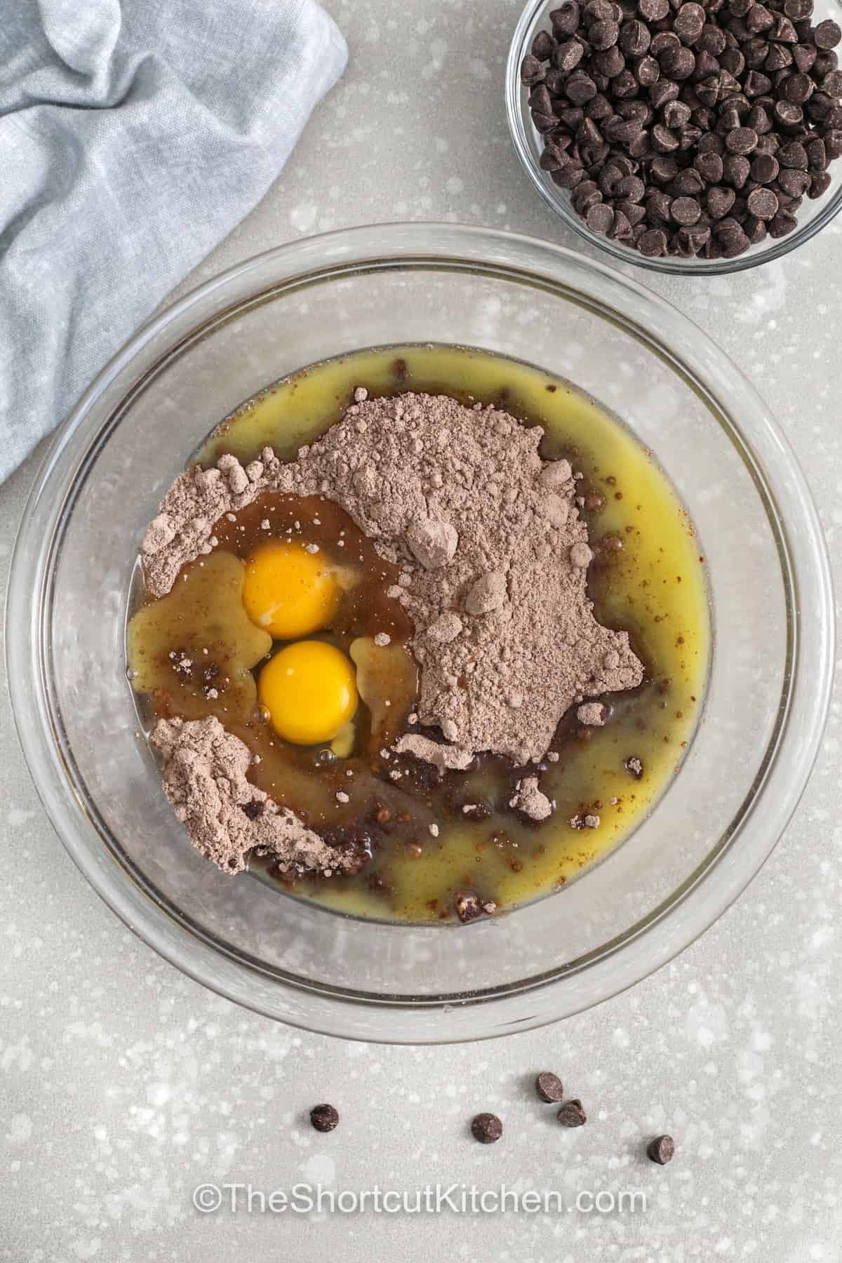 Chocolate cake cookie mix makes these cookies taste like the perfect cross between a fudgy brownie and a classic chocolate chip cookie. They bake up thick, soft, and full of deep cocoa flavor with pockets of melted chocolate in every bite. This shortcut recipe is ideal for busy days when you still want a warm, fresh baked dessert that feels special without much effort. #theshortcutkitchen adding egg and butter to cake mix batter to make Chocolate Cake Mix Cookies