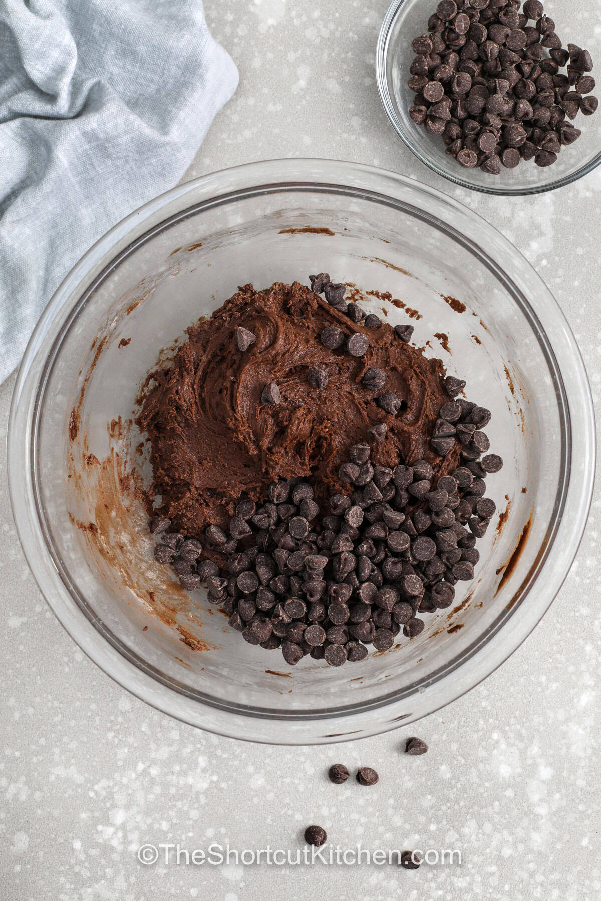 Chocolate cake cookie mix makes it possible to create indulgent cookies in just minutes using basic pantry staples. The result is a soft and chewy cookie with a rich chocolate base and plenty of melty chocolate chips scattered throughout. They stay tender for days, making them great for sharing, snacking, or packing into lunches as a sweet homemade treat everyone will love. #theshortcutkitchen adding chocolate chips to bowl to make Chocolate Cake Mix Cookies