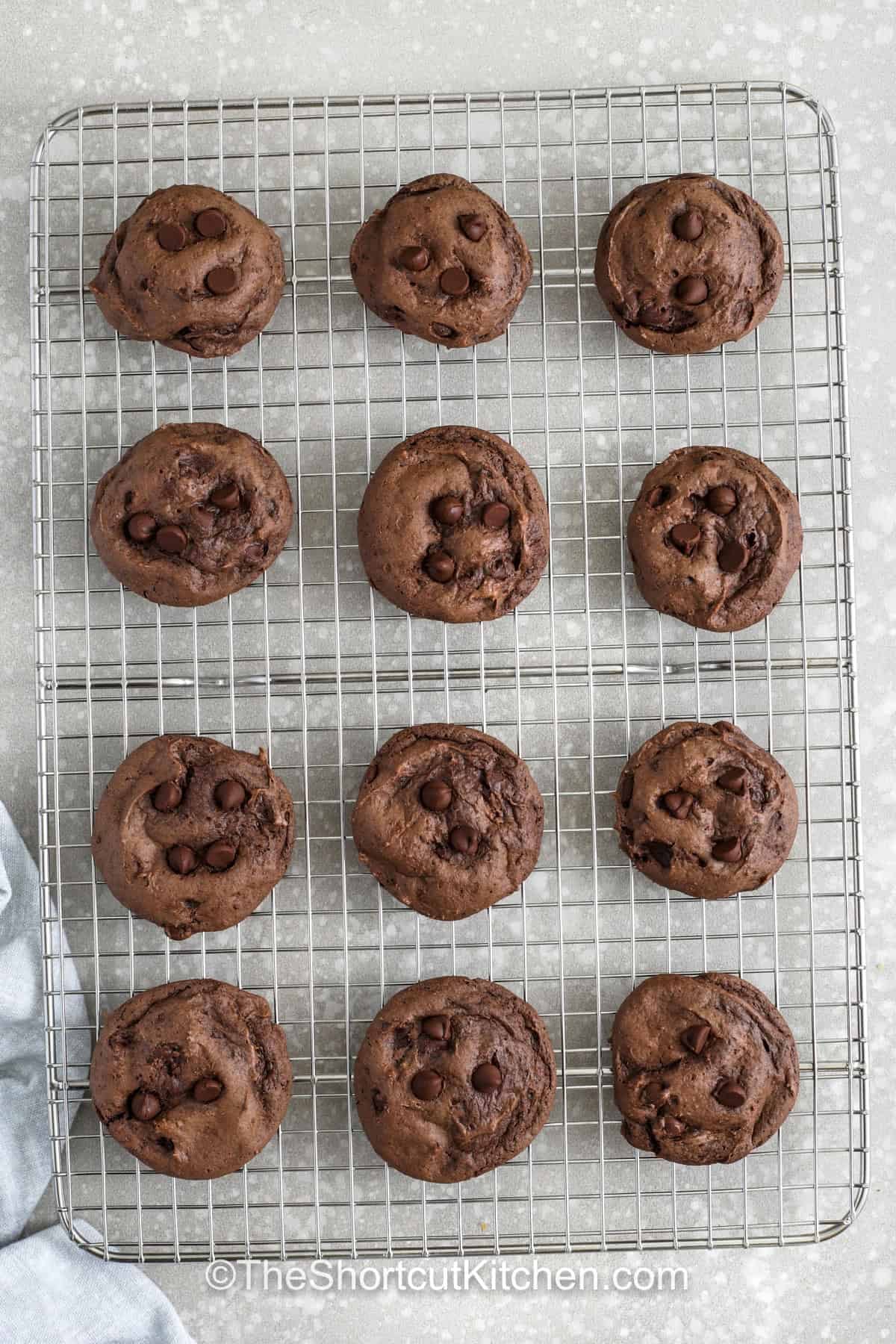 Chocolate cake cookie mix makes these cookies a go to shortcut for satisfying chocolate cravings fast with minimal ingredients and effort. The dough comes together quickly and bakes into soft, chewy cookies that are loaded with chocolate chips and rich cocoa flavor. They are perfect for last minute desserts, unexpected guests, or anytime you need a quick homemade sweet treat. #theshortcutkitchen top view of Chocolate Cake Mix Cookies on a cooling rack