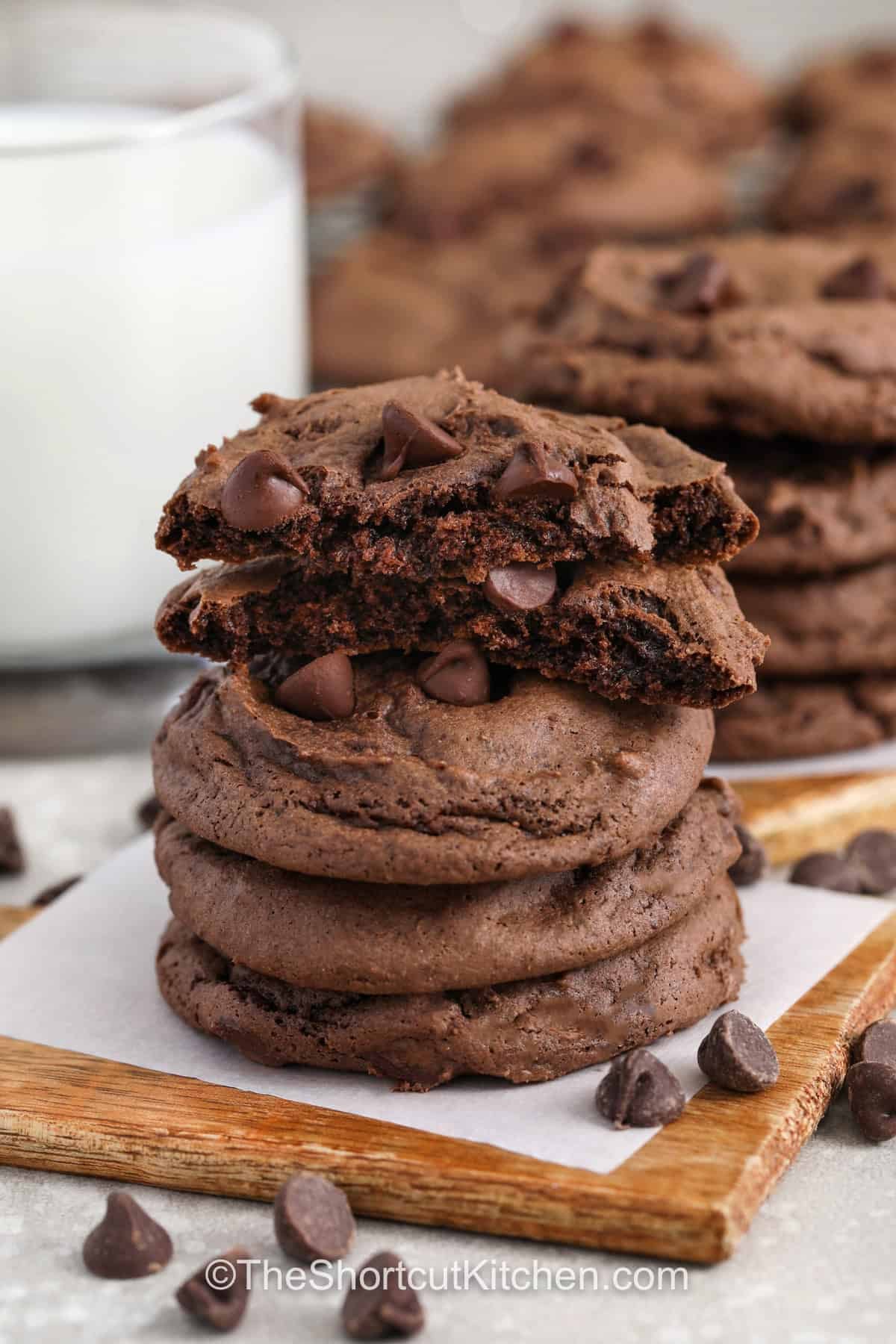 Chocolate cake cookie mix makes these cookies rich, soft, and deeply chocolate flavored with a fudgy brownie like center that stays tender for days. The simple ingredients come together in one bowl to create thick bakery style cookies loaded with melty chocolate chips in every bite. They bake up quickly with minimal prep, making them perfect for busy days when you still want a homemade dessert that feels indulgent and satisfying. #theshortcutkitchen stack of Chocolate Cake Mix Cookies with one in half to show middle