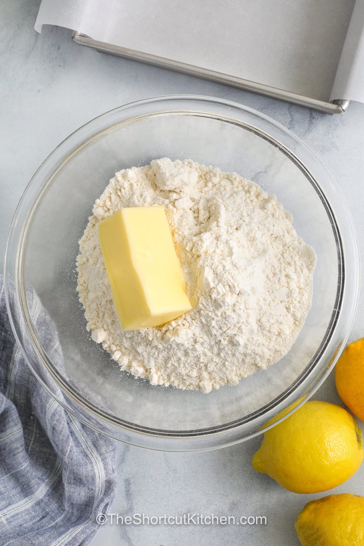 Easy lemon bars are a simple dessert made with a handy shortcut that still tastes homemade. A sugar cookie mix creates a quick crust, topped with a creamy layer of sweetened condensed milk, egg yolks, and fresh lemon juice. They bake in one pan, then chill until set and slice clean for parties, brunch, or holiday trays. Each bite has a bright lemon flavor that keeps them light and fresh. #theshortcutkitchen adding butter with dry ingredients to make Easy Lemon Bars