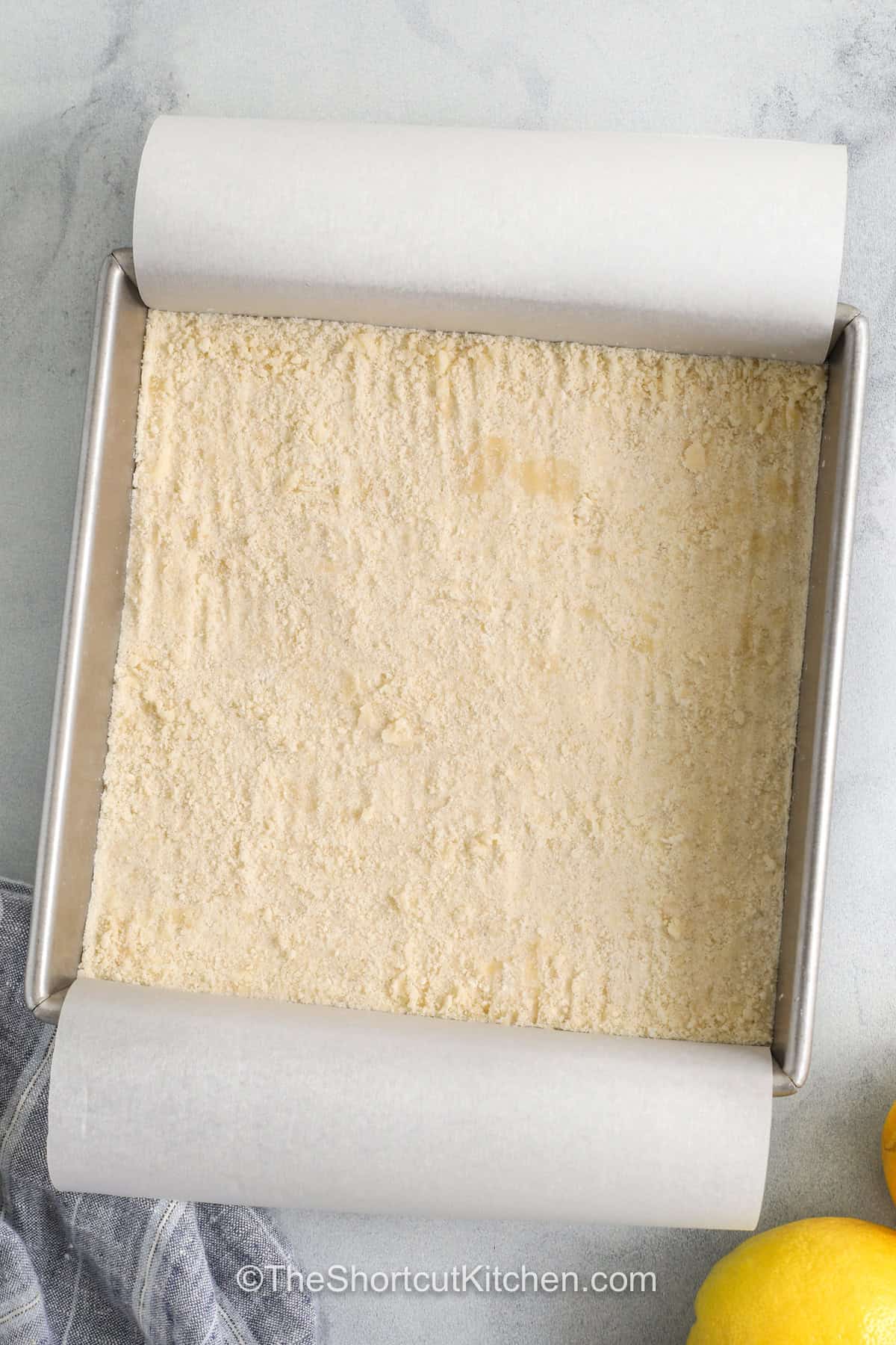 Easy lemon bars have bright citrus flavor and are simple to make at home. A cookie mix crust keeps prep easy, while fresh lemon juice gives a sweet and tangy taste to the creamy filling made with condensed milk. After baking and chilling, a light dusting of powdered sugar adds the perfect finish. These bars are easy to share and a great pick when you want a simple dessert with lots of flavor. #theshortcutkitchen adding crust to pan to make Easy Lemon Bars