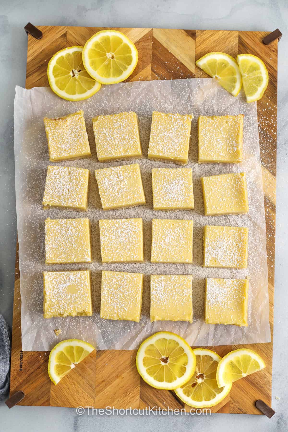 Easy lemon bars bring big citrus flavor without extra work. A cookie mix crust keeps things easy, while fresh lemon juice adds a bright, sweet tart taste to the creamy filling made with condensed milk. Once baked and chilled, they are finished with powdered sugar for a classic dessert that is easy to share and always a hit. They are a great choice when you want something simple but still full of flavor. #theshortcutkitchen Easy Lemon Bars on a cutting board with powdered sugar on top