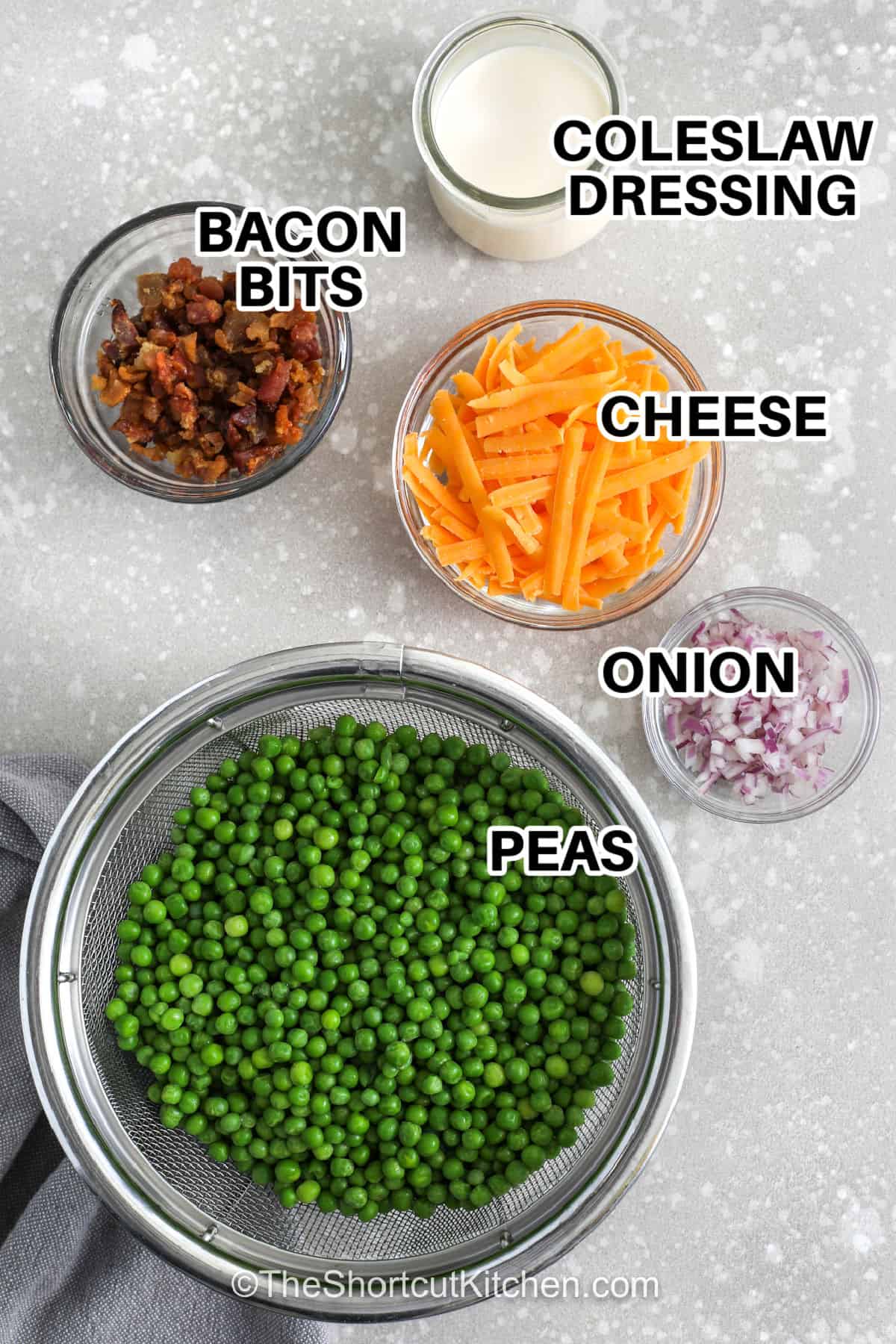 Pea salad with bacon is a simple cold salad recipe that delivers creamy, smoky, and tangy flavor in every bite. Made with frozen peas, cheddar cheese, bacon bits, and a quick dressing, this easy pea salad is ideal for potlucks and holiday menus. Use bottled dressing for a shortcut, or make the homemade version for a more classic pea salad with bacon flavor. #theshortcutkitchen coleslaw dressing , cheese , bacon bits , onion , peas with labels to make Pea Salad with Bacon