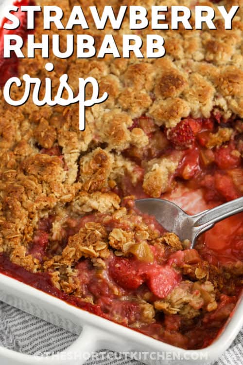Strawberry rhubarb crisp is a sweet and tangy dessert that is easy to love. Juicy strawberries and tart rhubarb bake together under a buttery cookie topping that turns golden in the oven. This simple fruit crisp uses a shortcut mix to keep prep easy while still tasting homemade. It is a great choice for spring and summer gatherings or a cozy dessert at home. Serve it warm with a scoop of ice cream for a classic finish everyone enjoys. #theshortcutkitchen taking a spoonful of Strawberry Rhubarb Crisp out of the dish with a title
