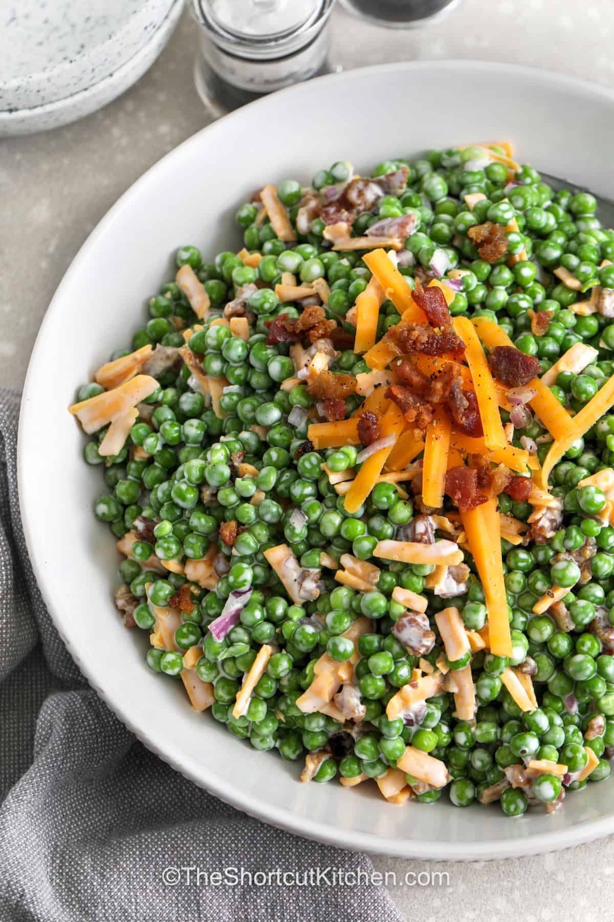 This creamy pea salad with bacon is made with everyday ingredients like frozen peas, cheddar cheese, bacon bits, and red onion, so it is easy to toss together anytime. It is a no-cook side dish with classic potluck flavor and a smooth, tangy dressing. Serve this pea salad recipe with grilled meats, sandwiches, or picnic favorites for a crowd-pleasing side everyone recognizes. #theshortcutkitchen close up of Pea Salad with Bacon