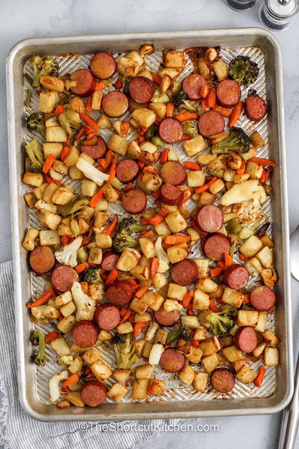 Sheet pan sausage and veggies make weeknight cooking simple and satisfying. Smoked sausage roasts alongside tender vegetables and crispy potatoes for a hearty one-pan dinner packed with flavor. The honey Dijon sauce adds a sweet and tangy finish that tastes great with every bite. Using frozen vegetables keeps prep easy while still making a colorful and comforting meal. Try this easy family dinner recipe for your next busy evening. #theshortcutkitchen top view of Sheet Pan Sausage and Veggies in the pan