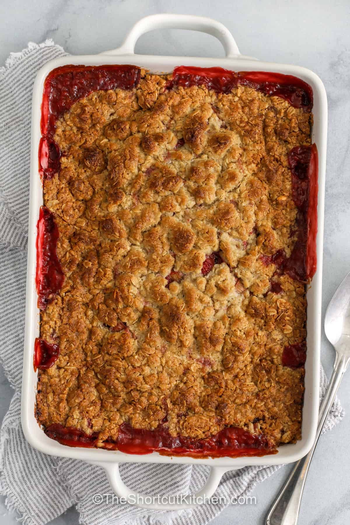 Strawberry rhubarb crisp is a sweet and tangy dessert that is easy to love. Juicy strawberries and tart rhubarb bake together under a buttery cookie topping that turns golden in the oven. This simple fruit crisp uses a shortcut mix to keep prep easy while still tasting homemade. It is a great choice for spring and summer gatherings or a cozy dessert at home. Serve it warm with a scoop of ice cream for a classic finish everyone enjoys. #theshortcutkitchen top view of Strawberry Rhubarb Crisp