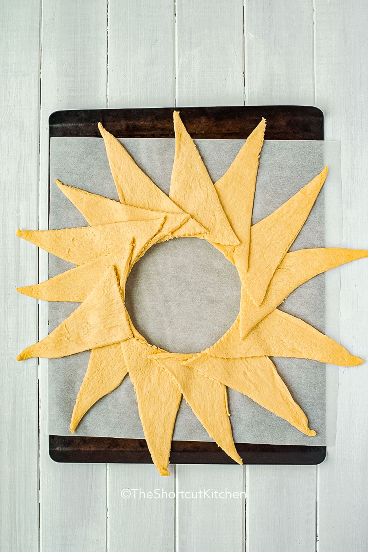 This cheesy taco ring recipe turns simple ingredients into a crowd-pleasing baked meal. It uses ground beef, taco seasoning, cheddar cheese, and refrigerated crescent rolls for a shortcut dinner that looks fun and festive on the table. A taco ring is perfect for taco night, game day snacks, or easy family meals with fresh toppings added just before serving. #theshortcutkitchen adding crescent roll slices to sheet pan to make Taco Ring