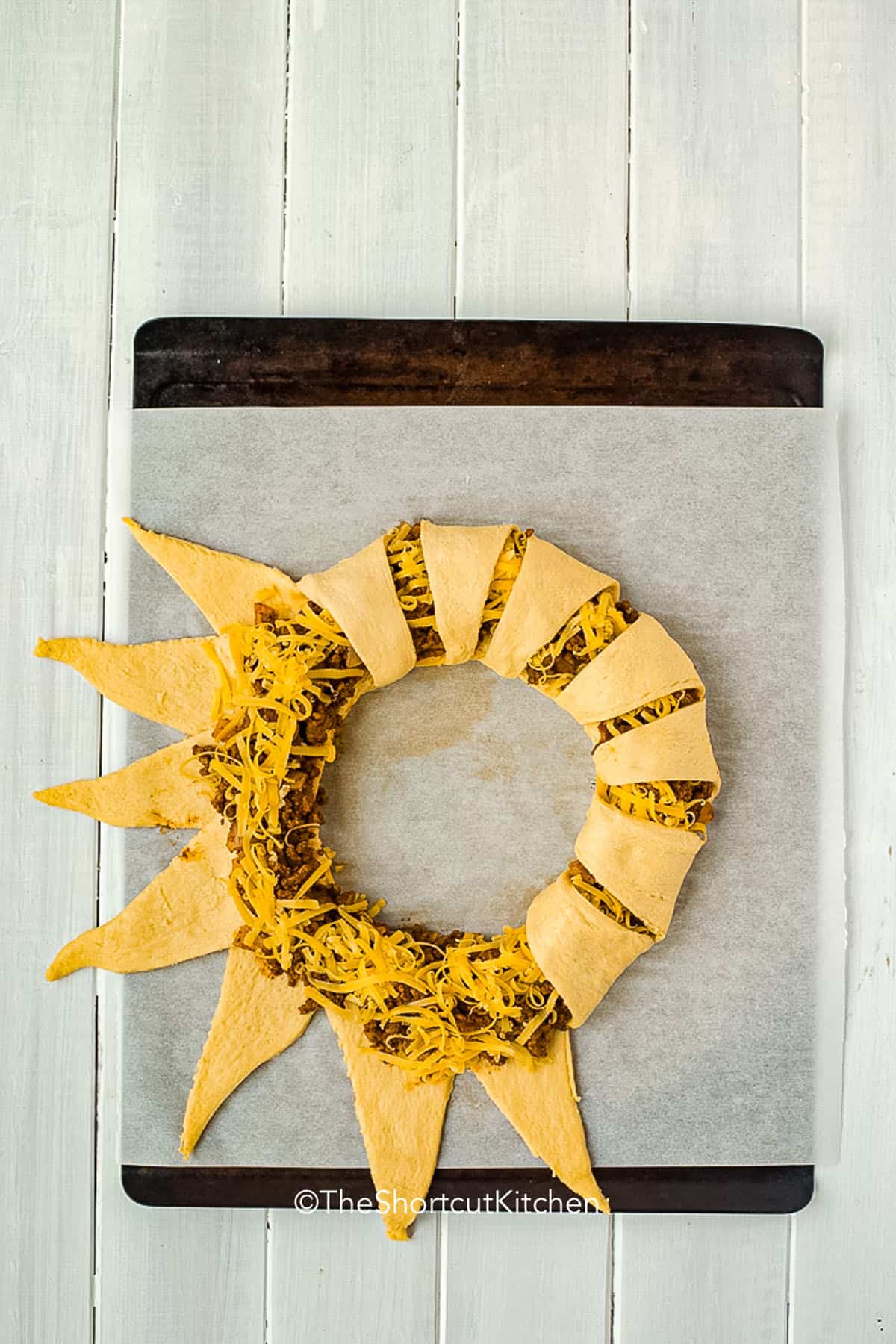 This taco ring is the kind of shortcut dinner that saves busy nights. Seasoned ground beef and cheddar cheese are wrapped in crescent rolls and baked until crisp and golden. This taco ring recipe is easy to customize with your favorite toppings and works for family dinners, game day, or casual parties when you want something warm, cheesy, and satisfying. #theshortcutkitchen folding over Taco Ring