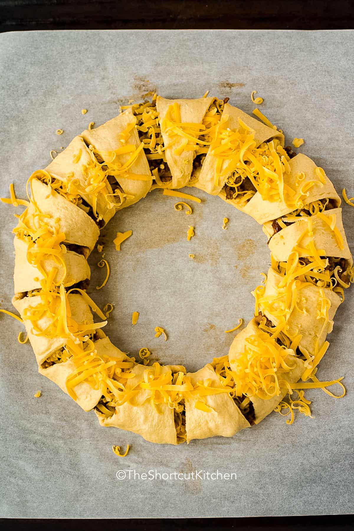 This Taco Ring recipe is an easy baked dinner made with ground beef, taco seasoning, cheddar cheese, and crescent rolls. It is a fun taco night twist that comes out golden, flaky, and ready to slice. Serve this ring with lettuce, tomatoes, sour cream, and salsa for a simple family dinner or party recipe that looks impressive without extra work. #theshortcutkitchen adding cheese to Taco Ring