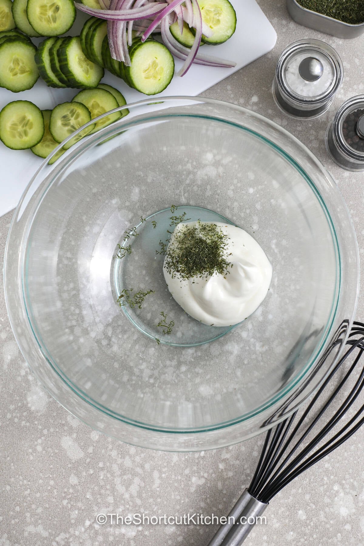 This creamy cucumber salad recipe is the perfect side dish for warm-weather meals and backyard cookouts. Crisp cucumbers and red onion are tossed in a creamy dill dressing with just the right tangy flavor. It pairs well with burgers, grilled chicken, sandwiches, and picnic favorites. Every bite is cool, fresh, and packed with simple homemade flavor. Keep this easy cucumber salad chilled and ready for dinner all summer long. Save this family favorite recipe today. #theshortcutkitchen adding dill and vinegar to sour cream to make dressing for Creamy Cucumber Salad Recipe