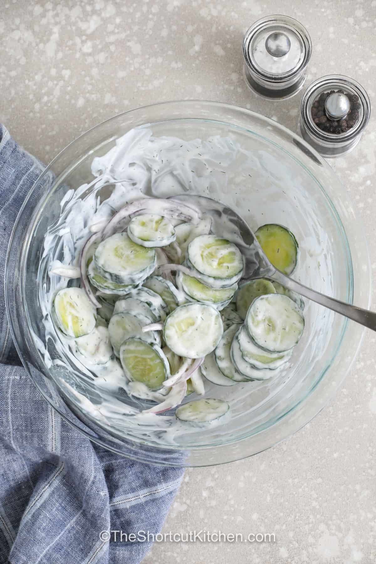 Looking for a fresh side dish everyone will love? This creamy cucumber salad recipe is filled with crisp cucumbers and creamy dill dressing that pairs perfectly with grilled meats and summer dinners. The mix of sour cream and vinegar gives this cucumber onion salad a bright flavor in every bite. It is easy to prepare ahead for cookouts, parties, and busy nights at home. Serve this chilled salad at your next family meal and watch it disappear fast. #theshortcutkitchen top view of Creamy Cucumber Salad Recipe ingredients mixed in a bowl