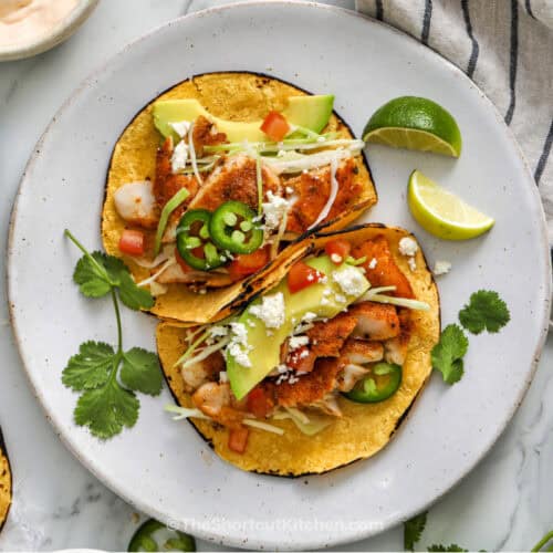 Cod Fish Tacos assembled on a plate with cilantro and quartered limes