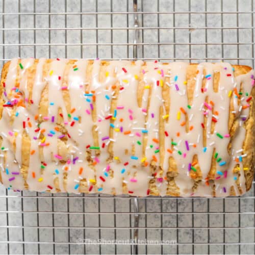 Delicious homemade funfetti cake roll with colorful sprinkles and white icing on a cooling rack.