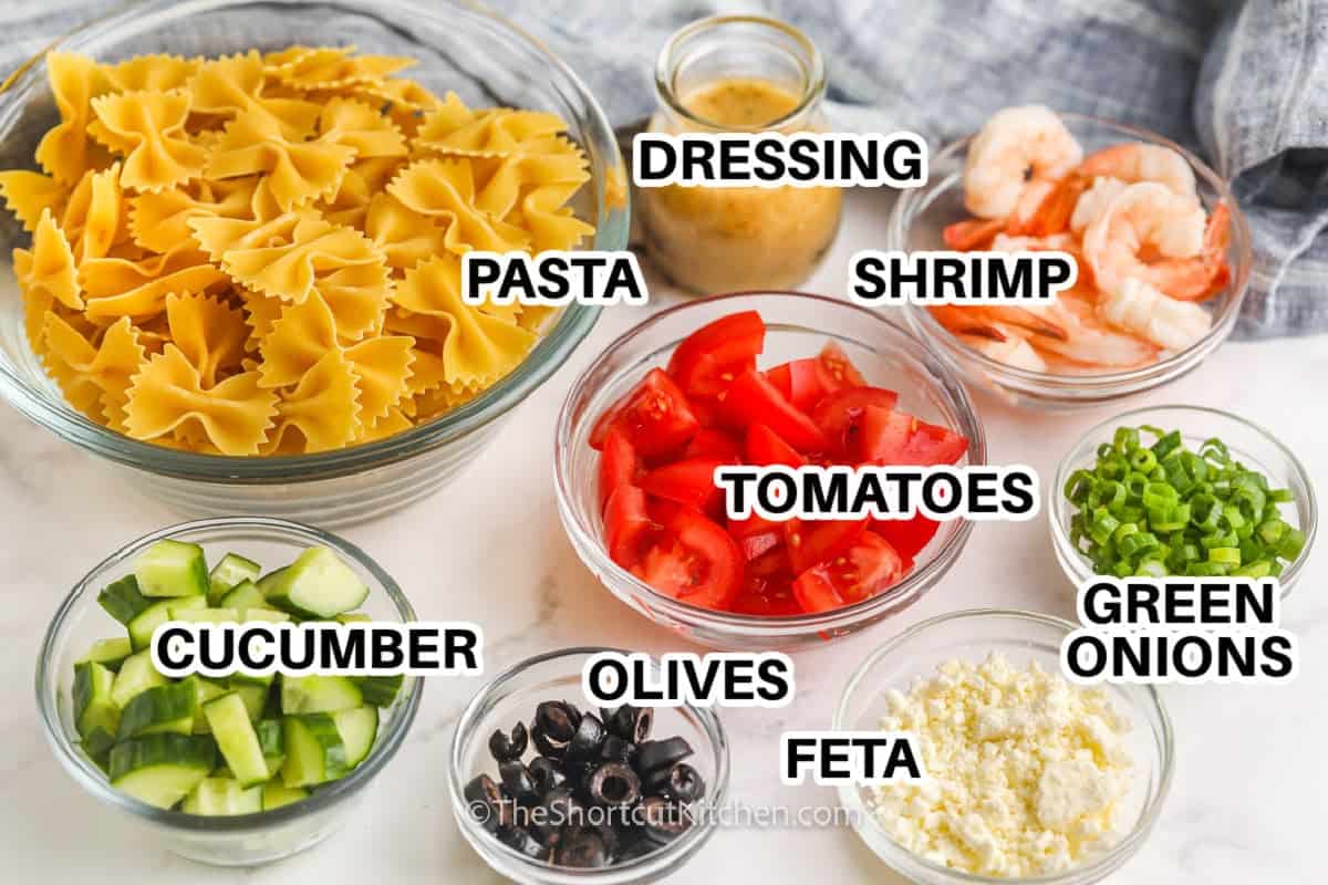 This easy Greek shrimp pasta salad is made with shortcut ingredients and classic Mediterranean-style flavors. Shrimp, pasta, feta, olives, cucumber, and tomatoes come together in a cold pasta salad recipe that is perfect for potlucks, lunches, and relaxed summer dinners. #theshortcutkitchen pasta , cucumber , olives , feta , green onions , tomatoes , shrimp and dressing with labels to make Greek Shrimp Pasta Salad