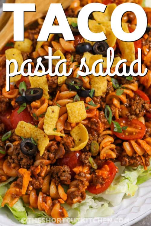 Make this easy taco pasta salad recipe for potlucks, BBQs, game day, or taco night. Tender rotini is tossed with taco-seasoned ground beef, cheddar cheese, green onions, juicy cherry tomatoes, and sweet tangy Catalina dressing. Serve it over crisp iceberg lettuce and top with corn chips or tortilla chips for a crunchy cold taco salad with pasta. #theshortcutkitchen plated Taco Pasta Salad on lettuce with writing